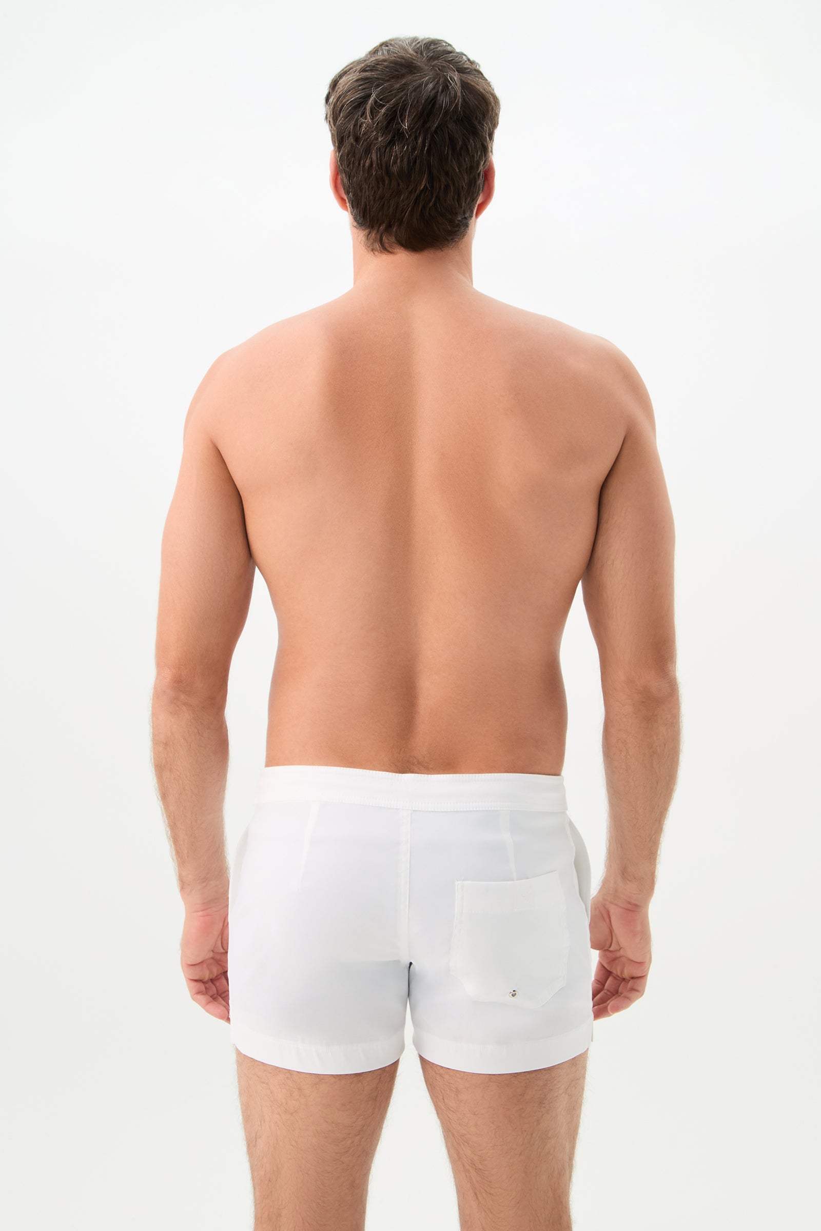 A man faces away from the camera, displaying his bare back and wearing Chico Swim Trunk - Lemar Solid in white with a back pocket, against a plain white background.