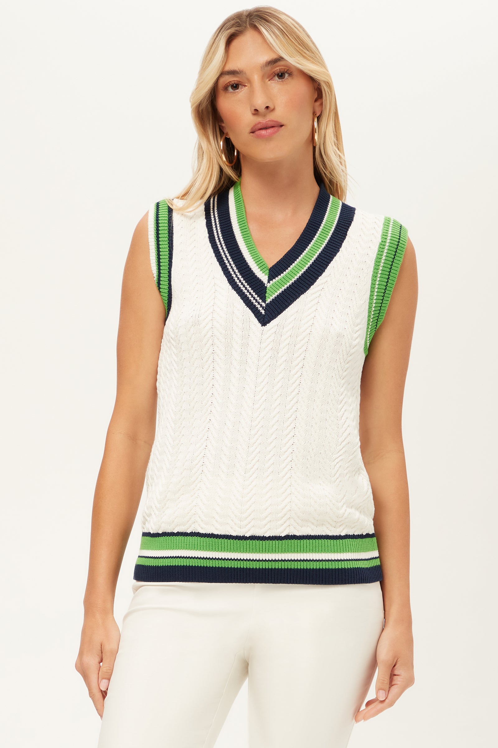 A woman wears the Seapointe 2 Sleeveless Knit Vest in Whitewash with navy and green stripes on the trim, styled with white pants, standing against a plain light background.