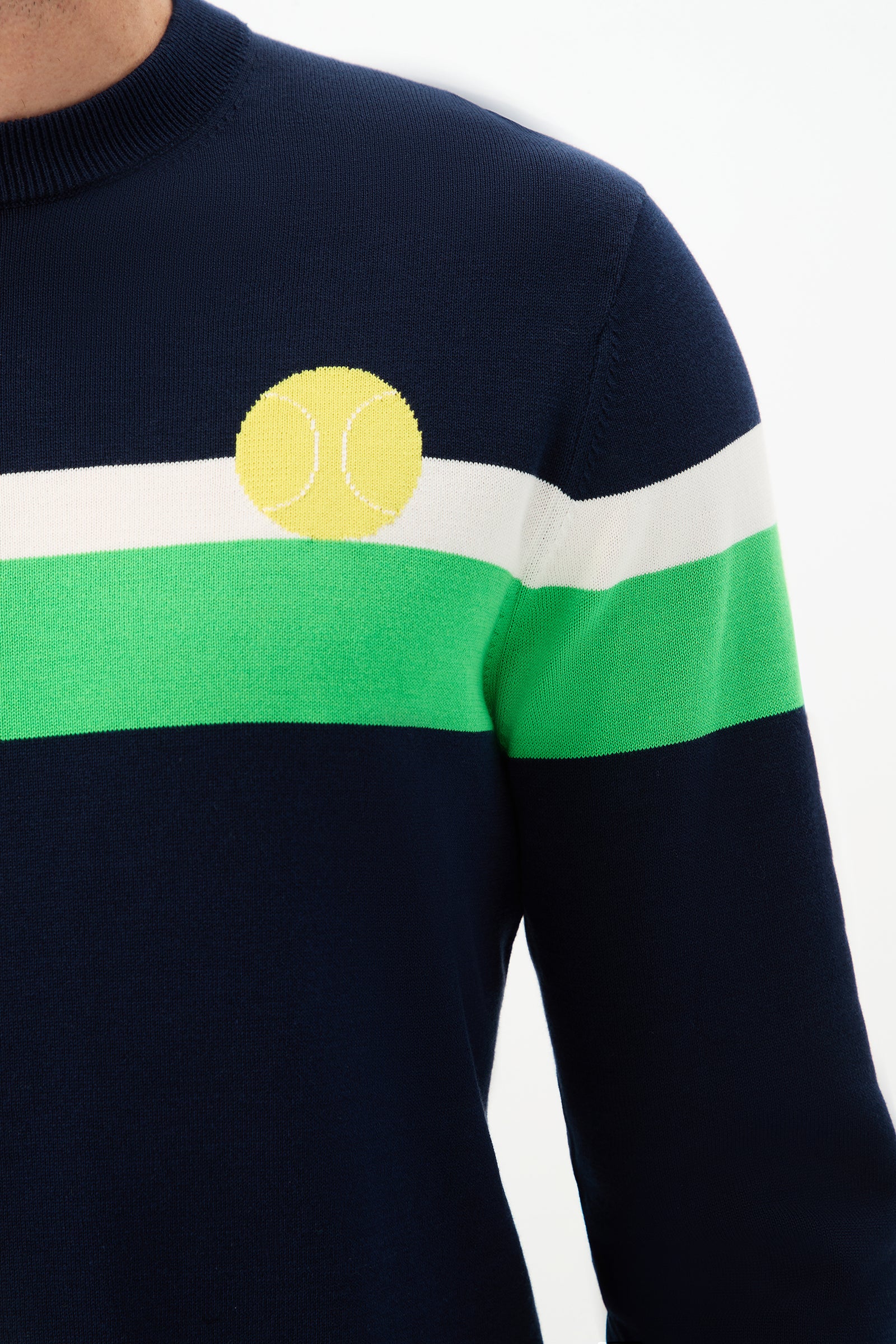 A person wearing the Romero Crewneck Sweater, featuring navy blue fabric with white and green horizontal stripes and a yellow tennis ball design on the chest.