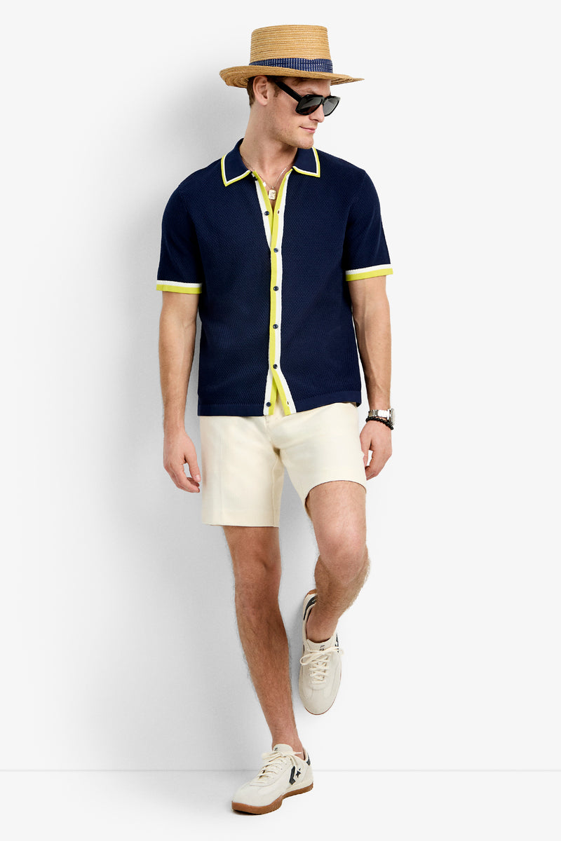 A man in the Kylian Short-Sleeve Polo, cream shorts, white sneakers, a straw hat, and sunglasses stands against a plain backdrop, looking to the side and smiling.