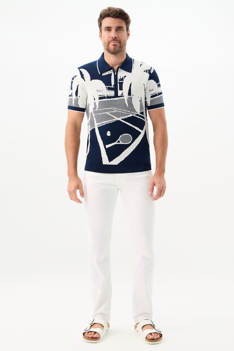 A man stands against a white background wearing the Grayson Short-Sleeve Polo - Graphic Knit featuring a white tennis court and palm tree design, paired with white pants and sandals.