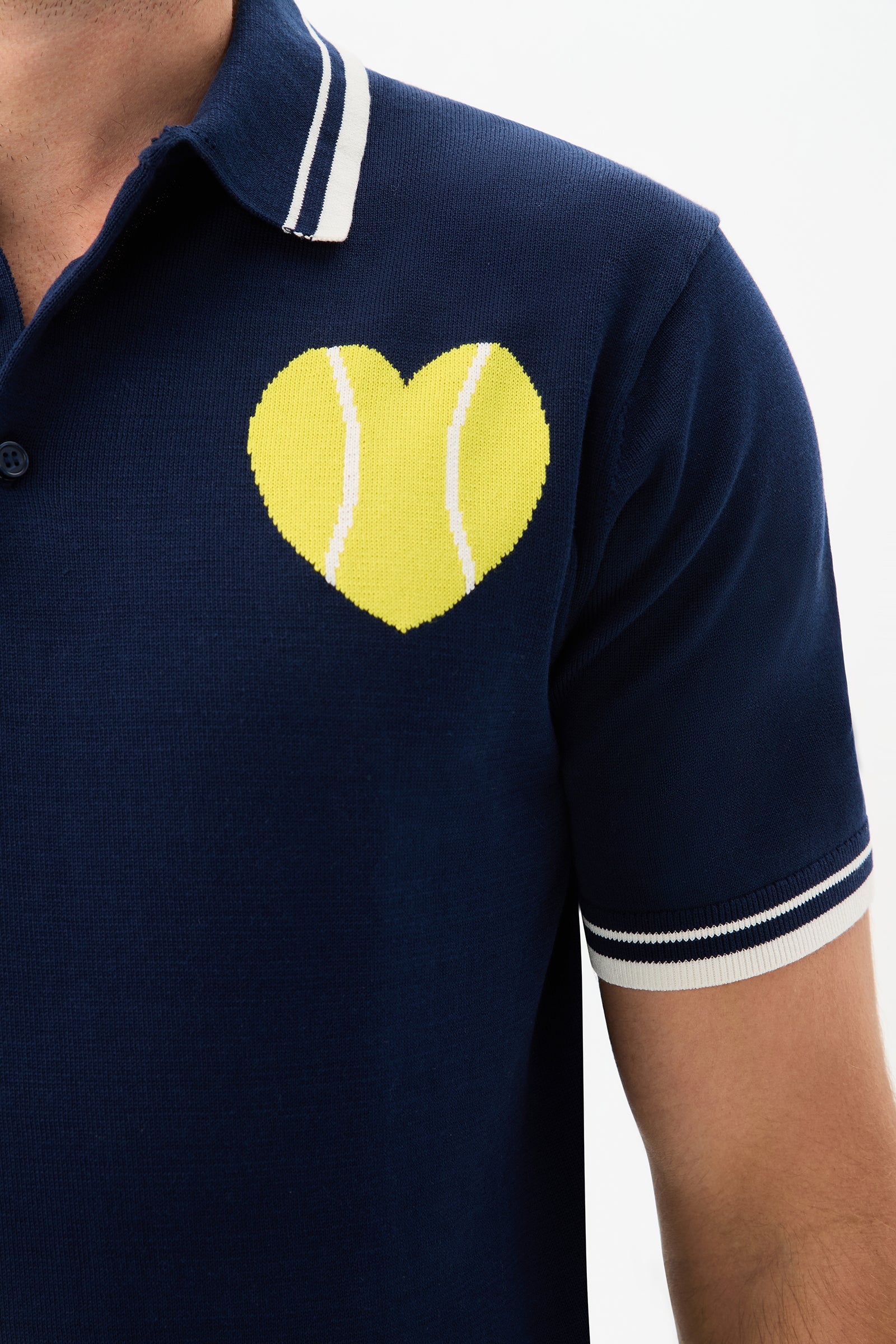 A person wearing the Tennis Heart Short-Sleeve Polo in navy blue, featuring white trim on the collar and sleeves and a yellow heart-shaped tennis ball design on the chest.