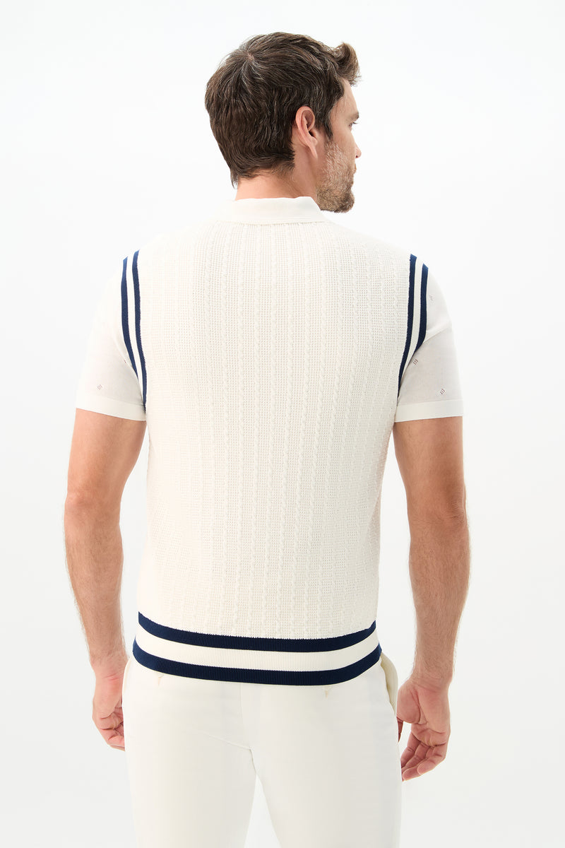 A man stands with his back turned, wearing the Matthew V-Neck Knit Vest in white with navy blue shoulder and hem stripes, paired with white pants against a plain white background.