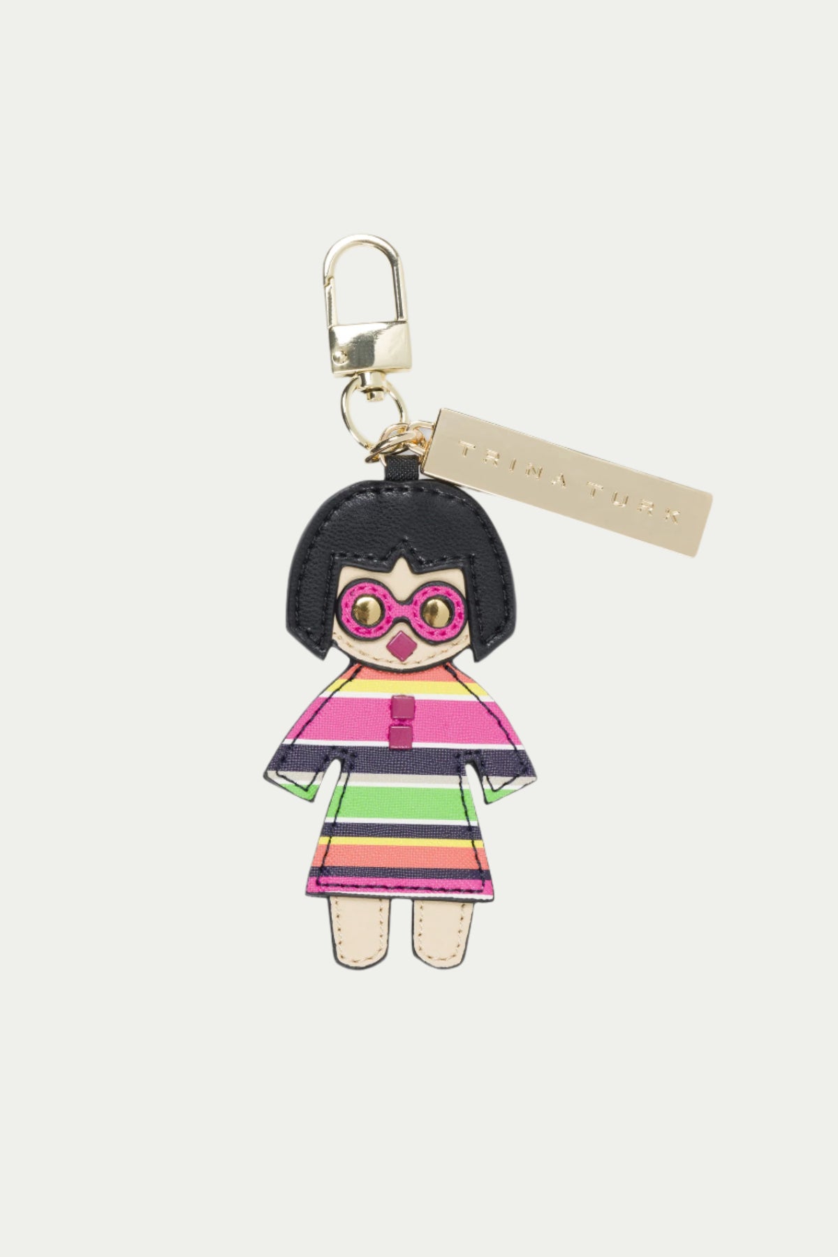 The Trina Key Charm - Splash Stripe is a colorful, multi-hued keychain featuring a cartoon figure with black hair, large pink glasses, and a striped dress, attached to a gold clasp and rectangular gold tag.