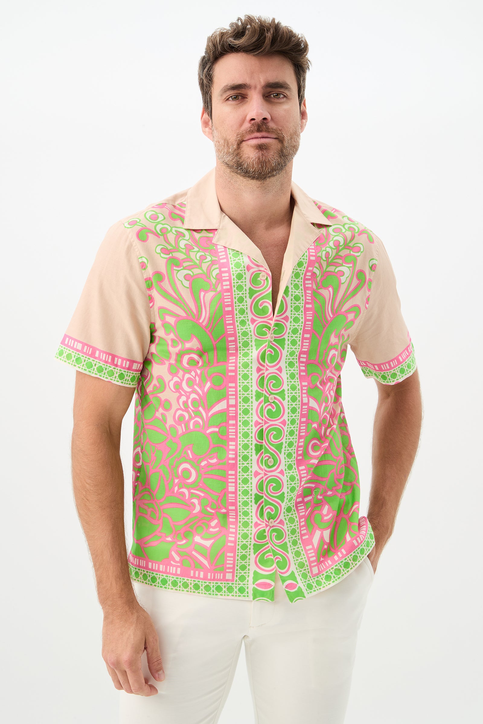 A man with short brown hair and a beard wears the Josue Short-Sleeve Shirt in Petra Floral, paired with white pants, standing against a plain white background.