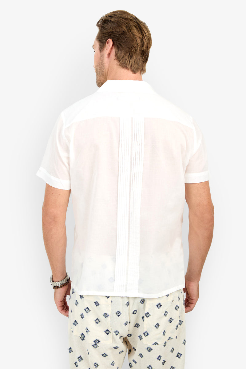 A man faces away, wearing the Allende Short-Sleeve Shirt in white with vertical back pleats and light-patterned shorts, standing against a plain white background.