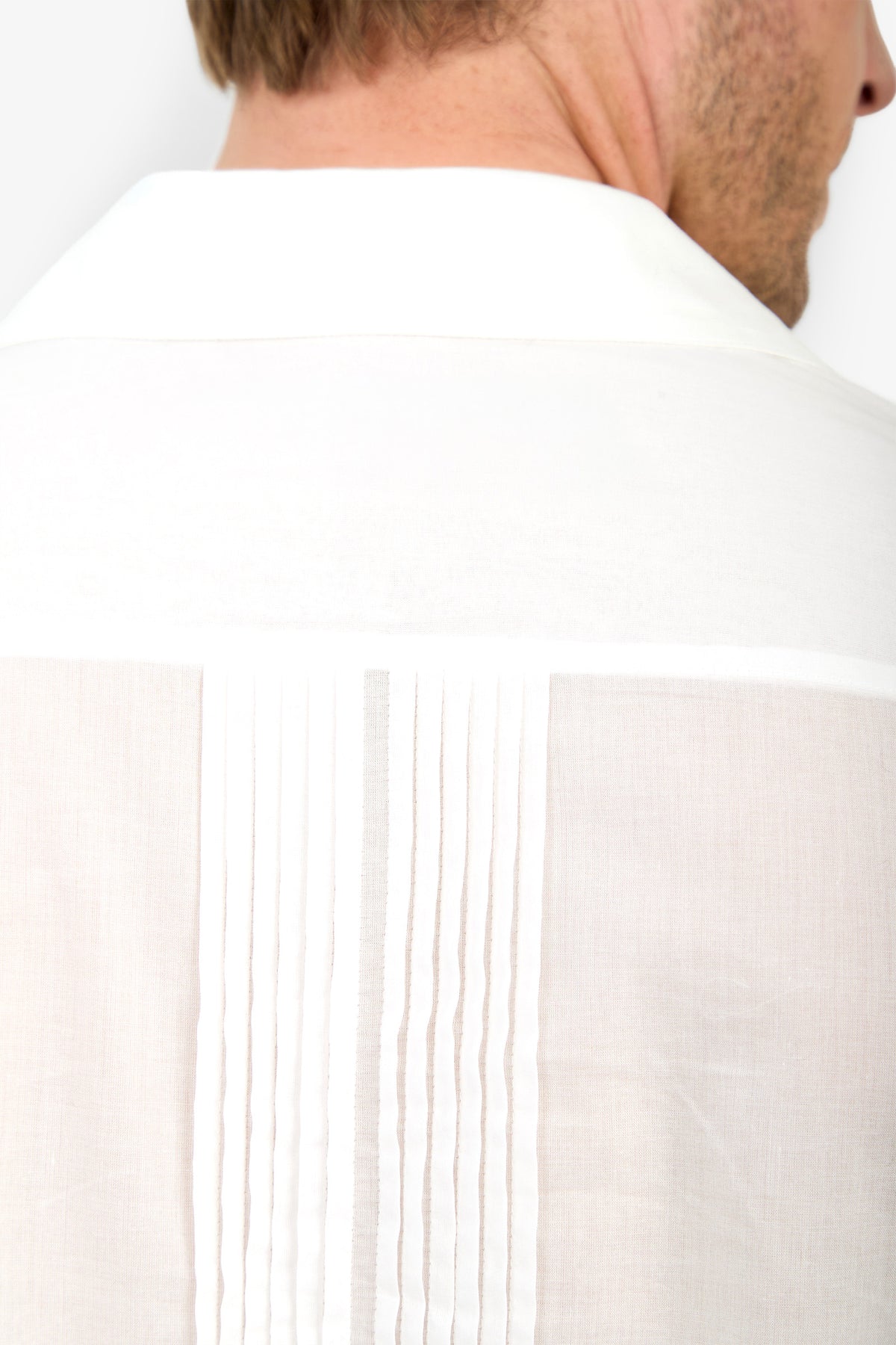 Close-up of the back of a person wearing the Allende Short-Sleeve Shirt in white, featuring vertical pleats and a collar. The person’s neck and short brown hair are visible.