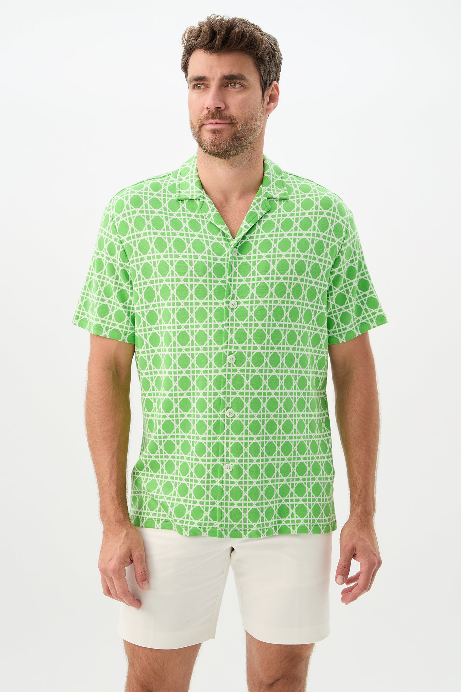A man with short brown hair and a beard wears the Felix Short-Sleeve Knit Shirt in Billie Jean, paired with white shorts, standing against a plain white background.