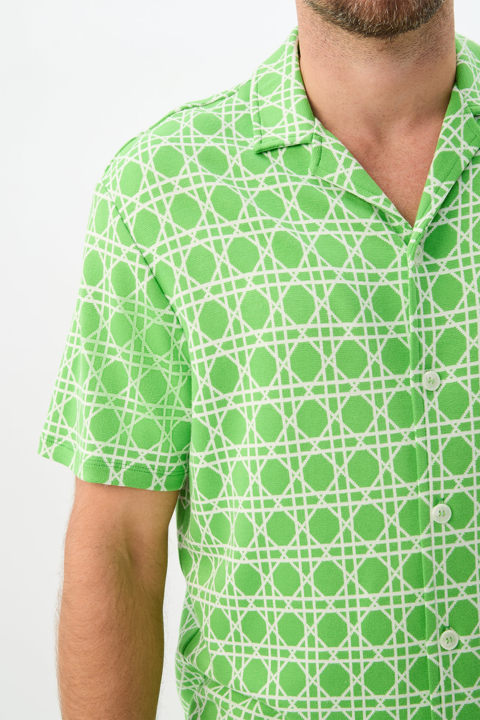 A man models the Felix Short-Sleeve Knit Shirt in Billie Jean, featuring a green and white geometric pattern, shown from shoulders to waist against a plain white background.