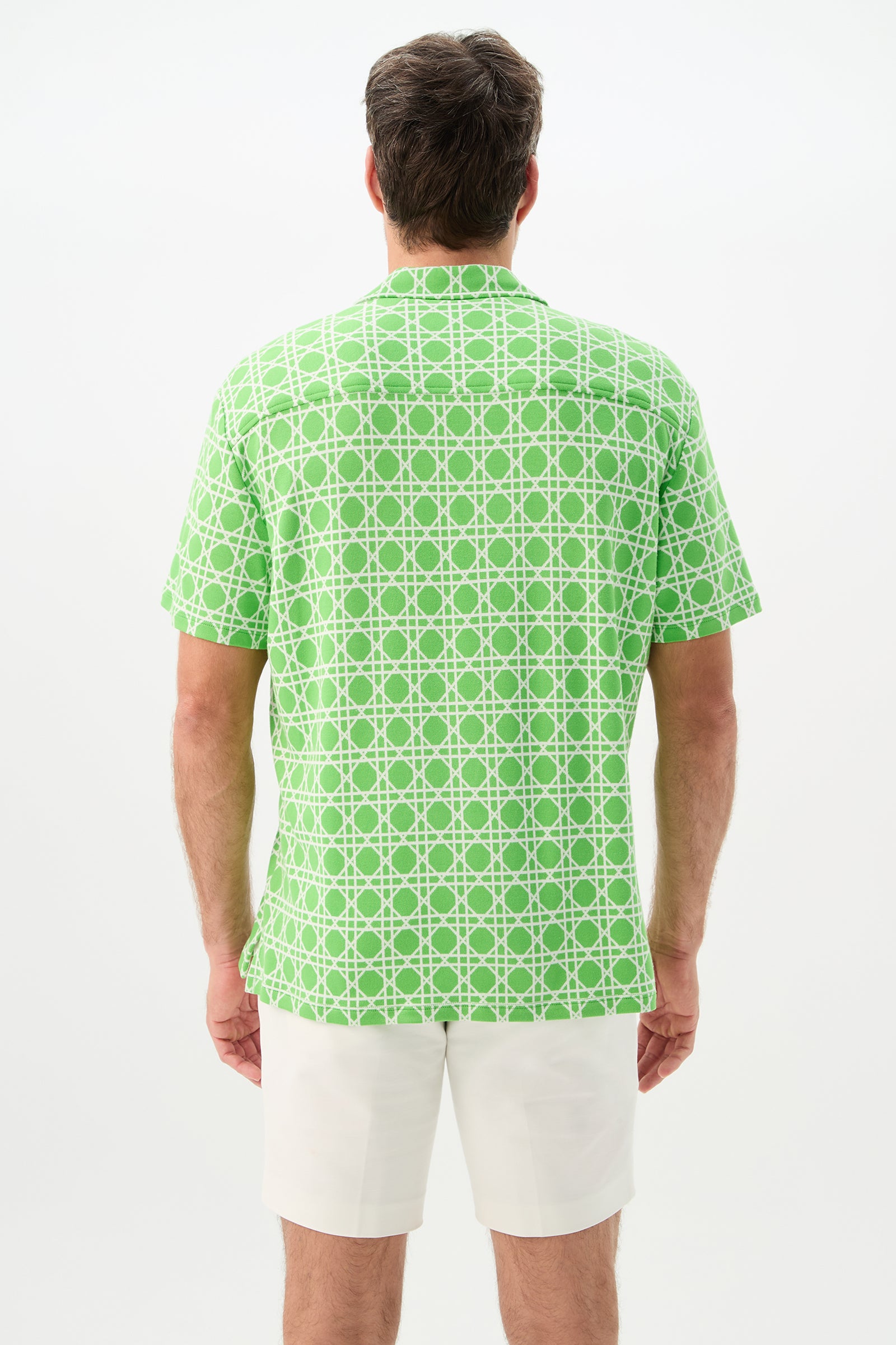 A man faces away, wearing the Felix Short-Sleeve Knit Shirt in Billie Jean—green with a white geometric pattern—and white shorts, set against a plain white background.