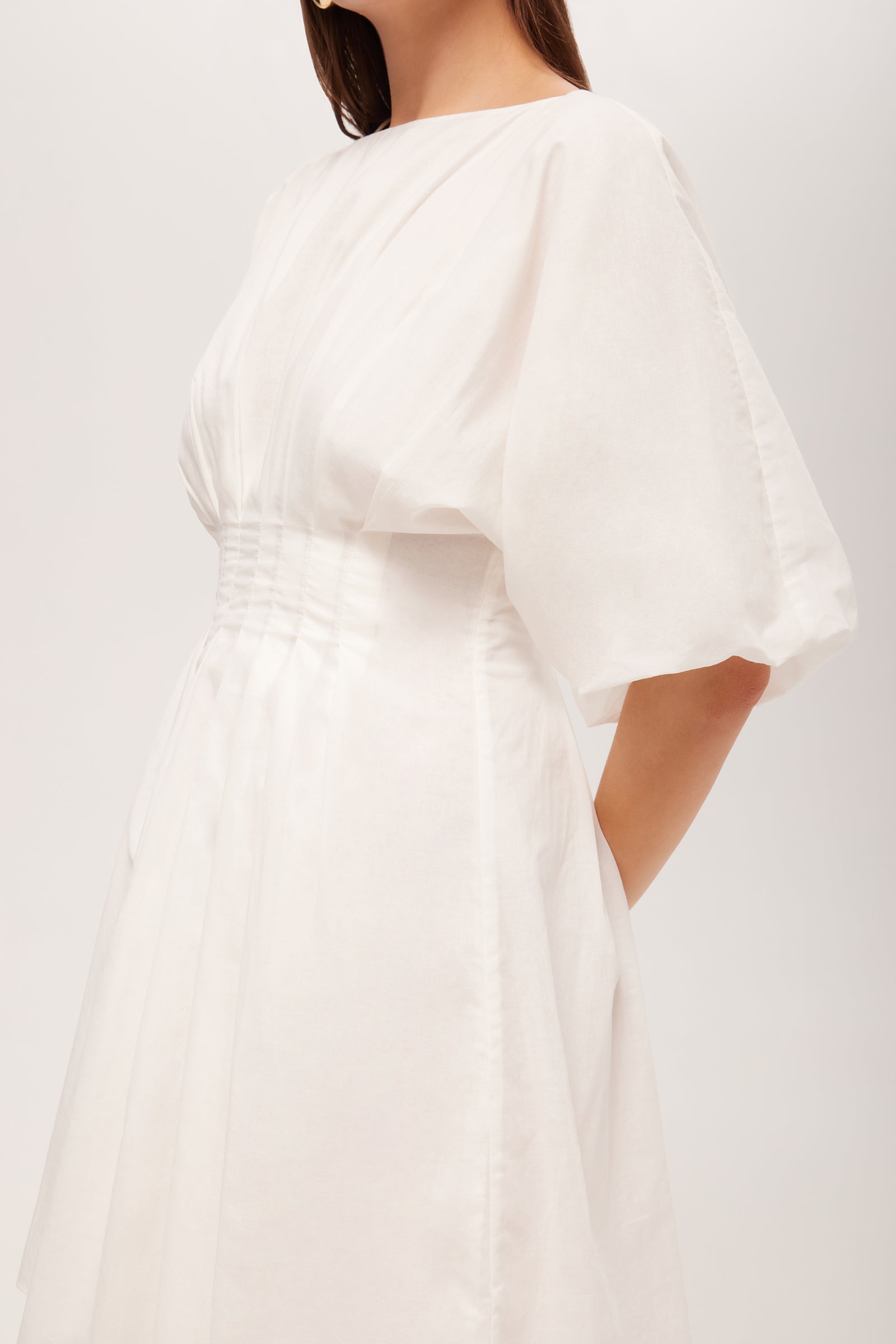 A woman wearing the Gian 2 Short-Sleeve Pleated Dress, featuring a fitted waist and flowing skirt, stands against a plain background with her face not visible.