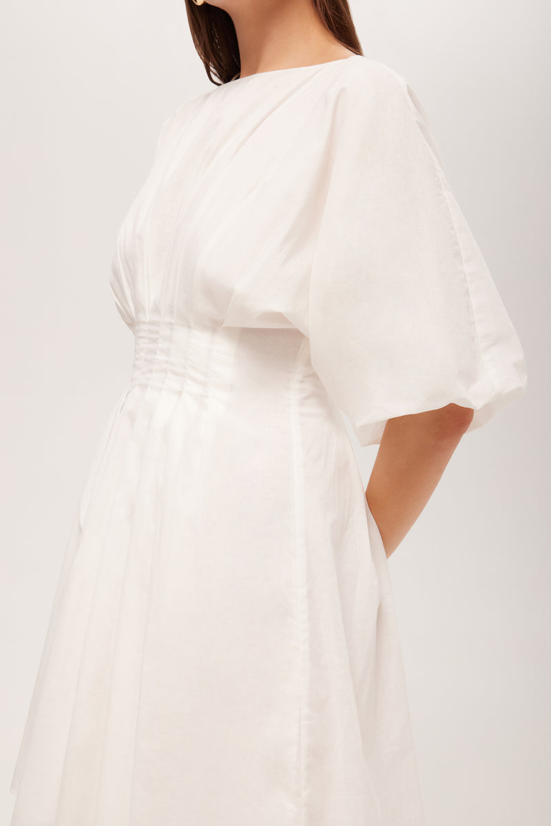A woman wearing the Gian 2 Short-Sleeve Pleated Dress, featuring a fitted waist and flowing skirt, stands against a plain background with her face not visible.