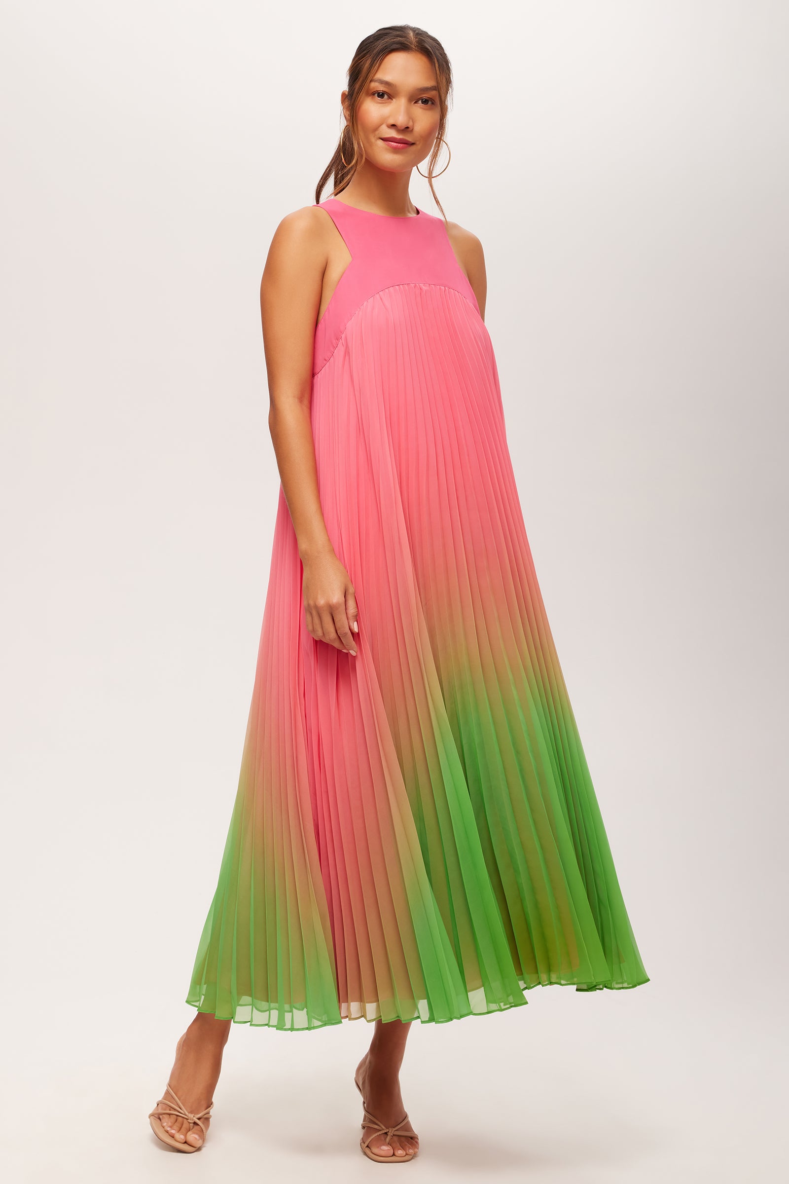 A woman wears the Jalina 2 Sleeveless Pleated A-Line Midi Dress in multi, featuring a pleated design and gradient color, paired with strappy sandals.