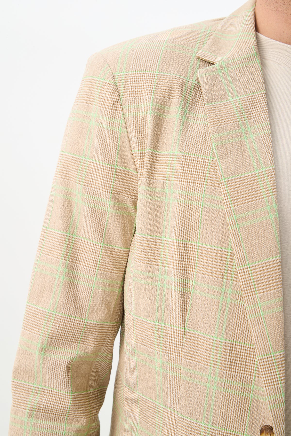 A close-up of the Louie Blazer - Zianieri Plaid, featuring a beige plaid with green lines over a light shirt. The image highlights the shoulder, collar, and upper chest area of the blazer.