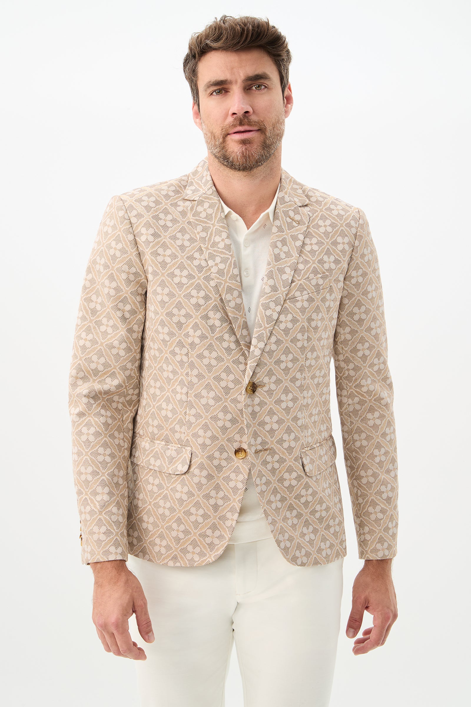 A man with short brown hair and a beard wears the Thurston Blazer in Beach Metallic Daisy Jacquard over a white shirt and white pants, standing against a plain white background.