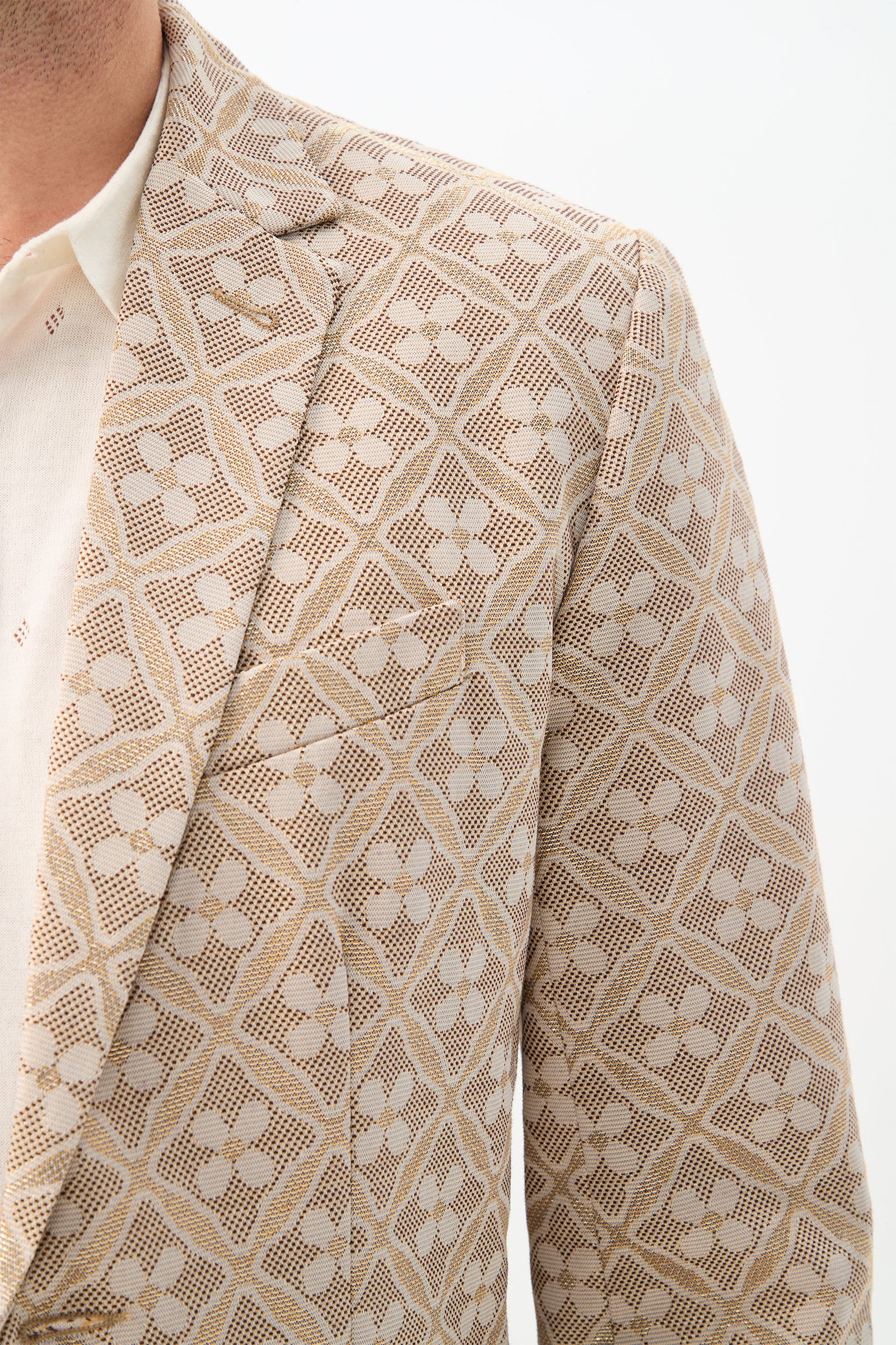 A close-up of a man wearing the Thurston Blazer in Metallic Daisy Jacquard over a cream shirt, shown from shoulders to mid-chest against a white background.