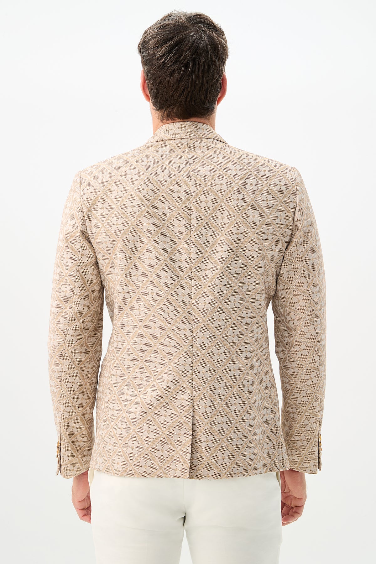 A man is seen from behind wearing the Thurston Blazer - Metallic Daisy Jacquard with white pants, standing against a plain white background.