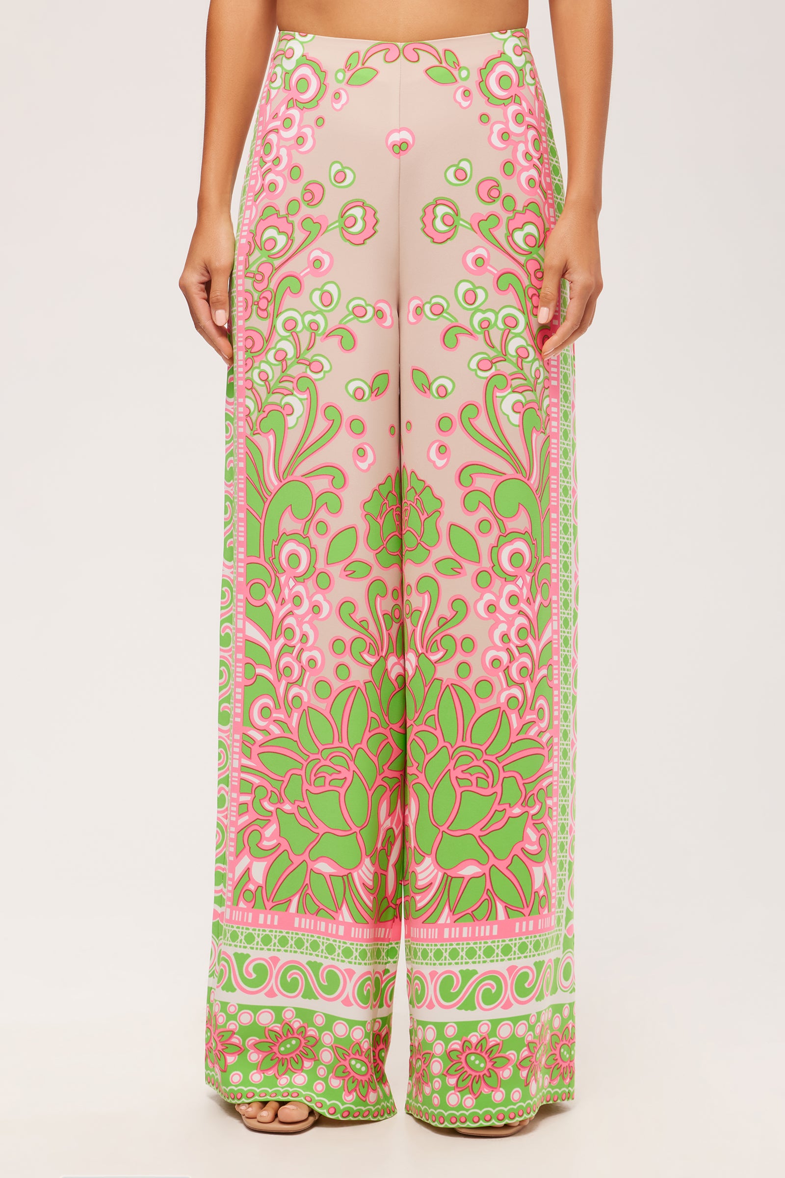 A person wearing the Federer Wide-Leg Pant - Petra Floral, featuring a high waist, flowing relaxed fit, and pink and green floral and geometric patterns on a light background.