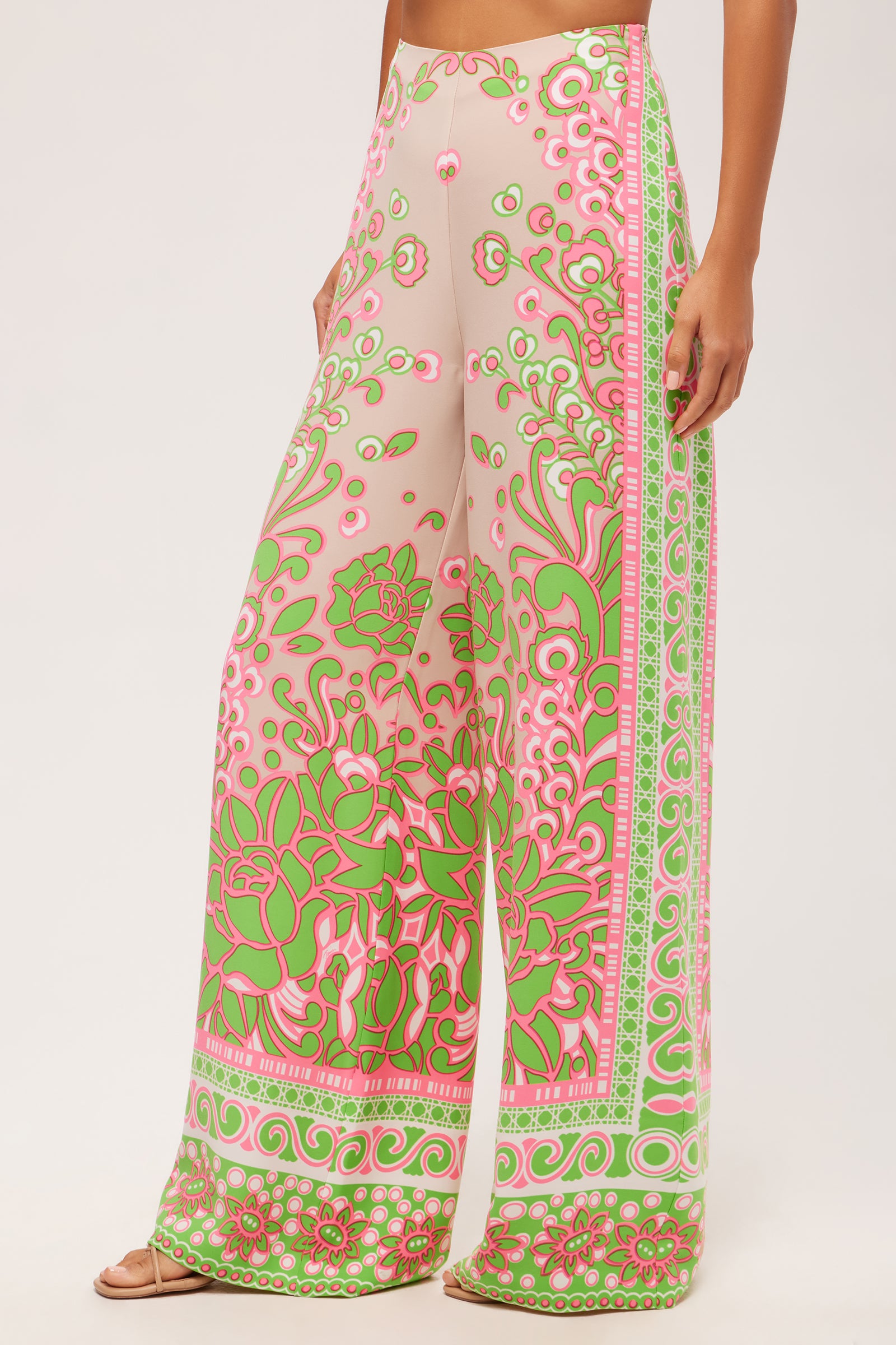 A person wearing the Federer Wide-Leg Pant in Petra Floral—a high-waisted, wide-leg style with a pink, green, and white floral and geometric pattern. The pants are floor-length and the person is barefoot.