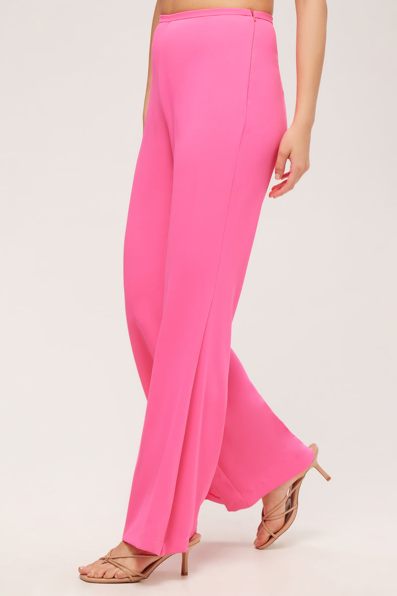 A person models the Drop Shot Flared Pant - Double Georgette in bright pink with nude heeled sandals, standing against a plain light background. Only the lower half of their body is shown.