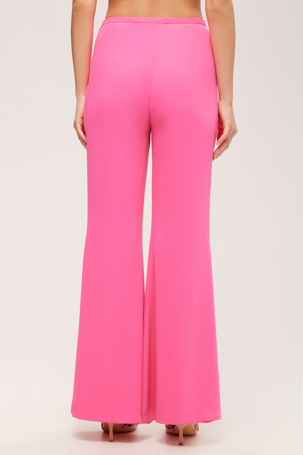 A woman is seen from behind wearing the Drop Shot Flared Pant - Double Georgette, a high-waisted, bright pink, wide-leg pant, standing against a plain light background.