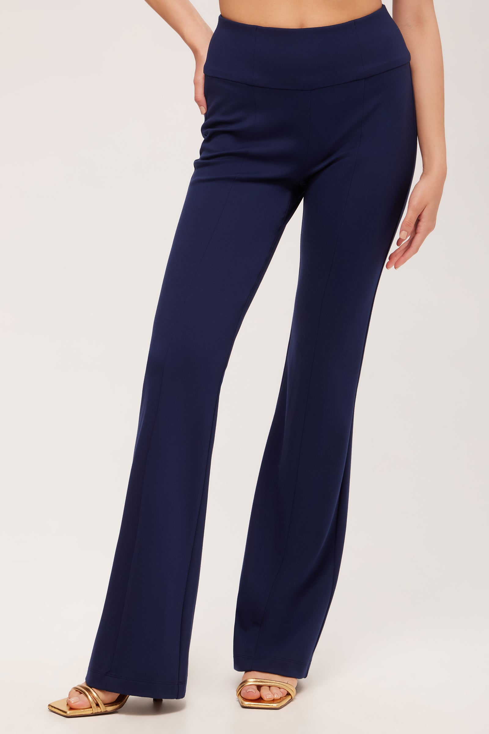 A person wears Becker High-Waist Flared Pant - Cozy Ponte in Ink with gold open-toe heels, standing against a plain light background.