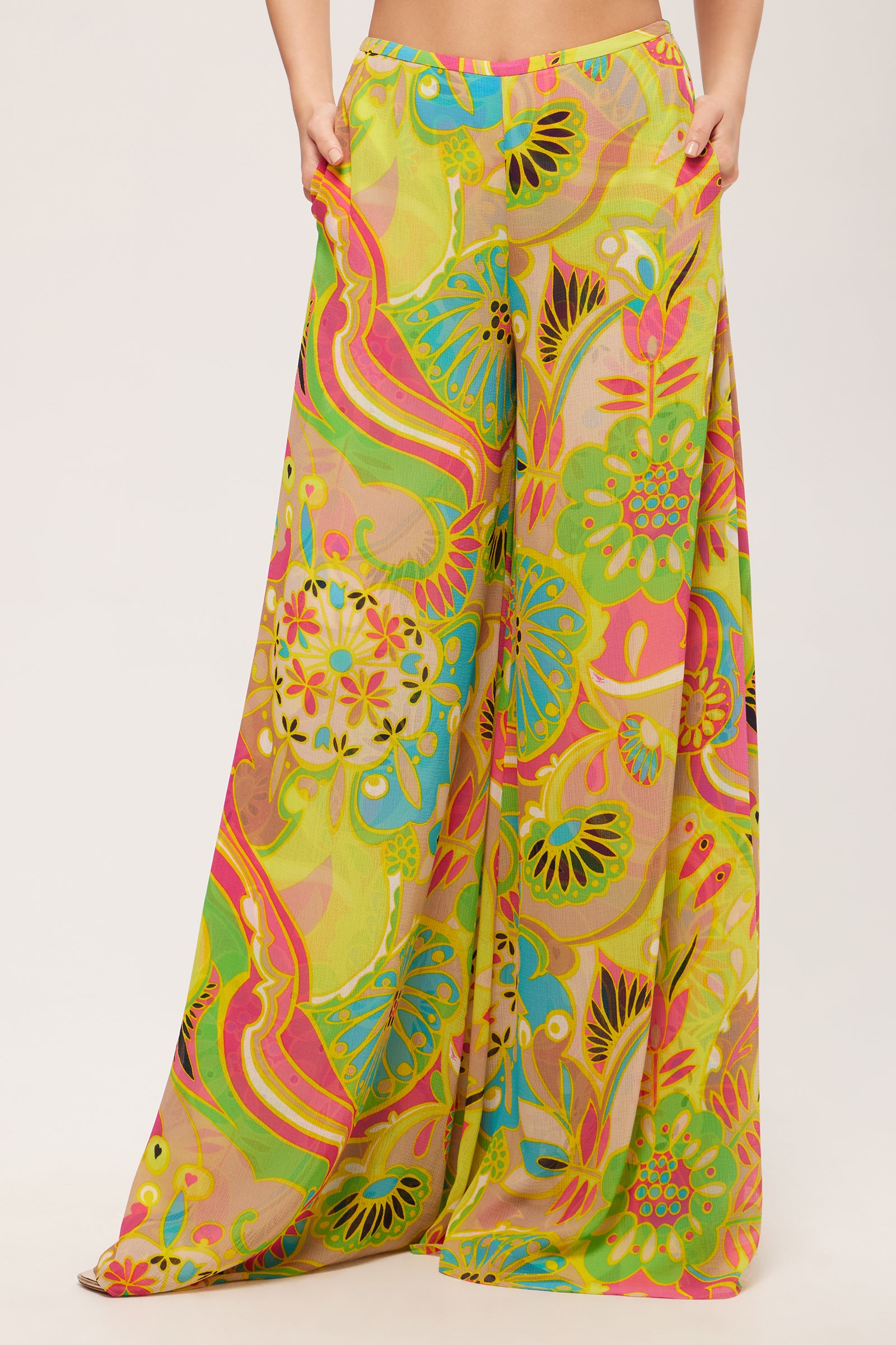 Woman wears the Jack Wide-Leg Pant in Venus, featuring a flowy, high-waisted fit and a vibrant multicolored abstract floral pattern in shades of green, yellow, pink, and orange against a plain background.