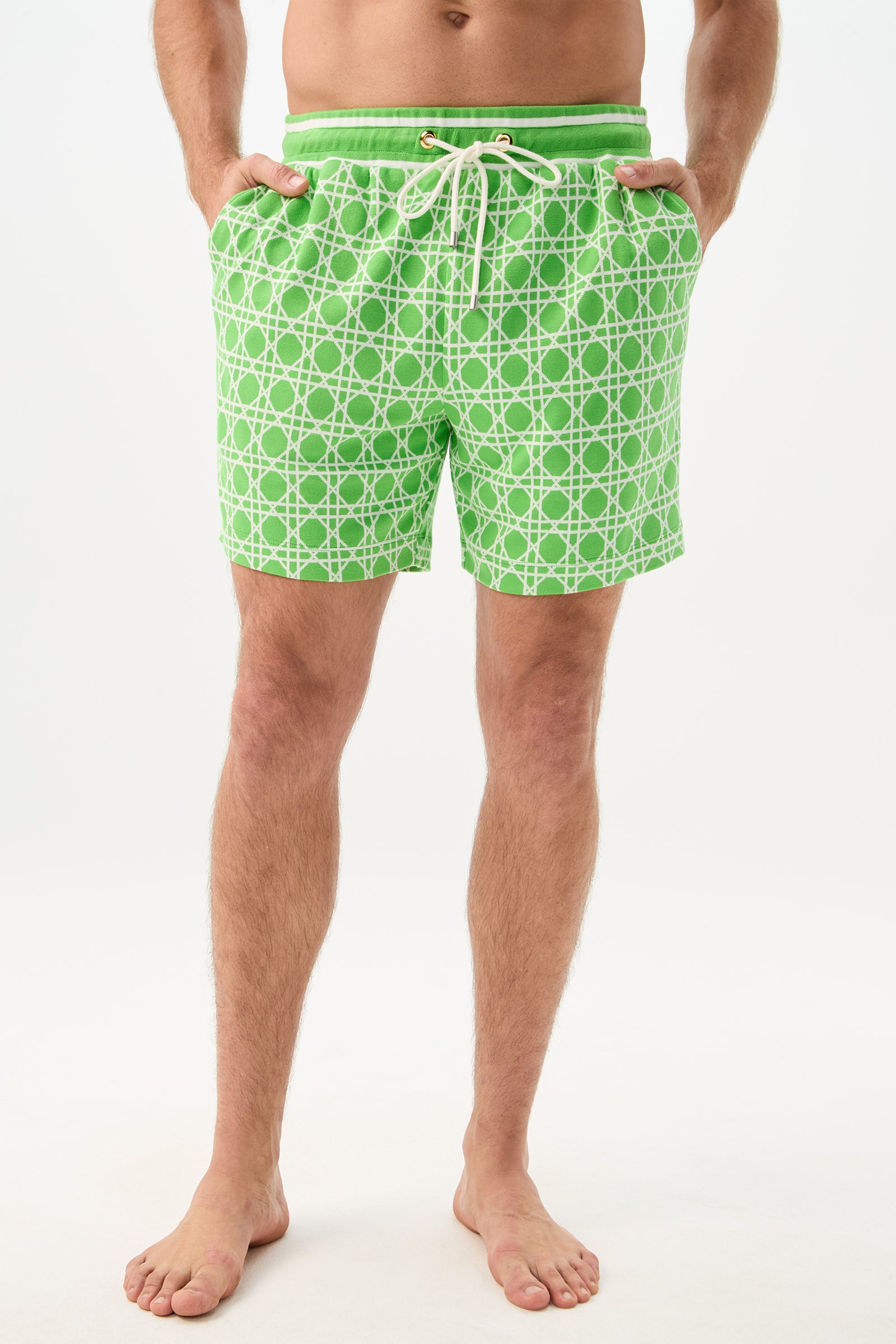 A man stands barefoot with hands in pockets, wearing Lounge Short - Billie Jean in the Billie Jean color, featuring a white geometric pattern and drawstring waist, against a plain white background.