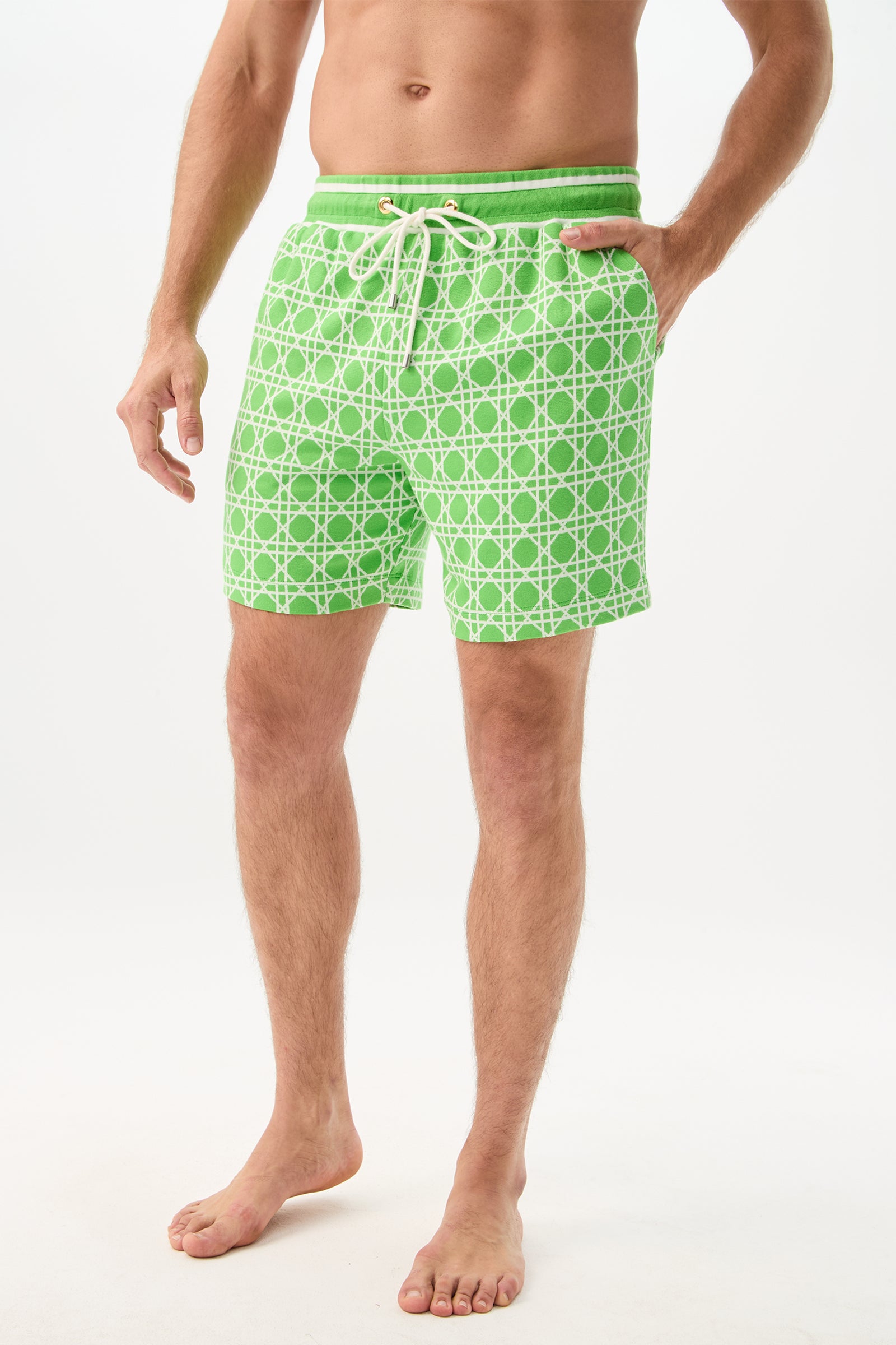 A man stands barefoot with his hands in the pockets, wearing the Lounge Short - Billie Jean, featuring light green patterns and white drawstrings, against a plain white background.