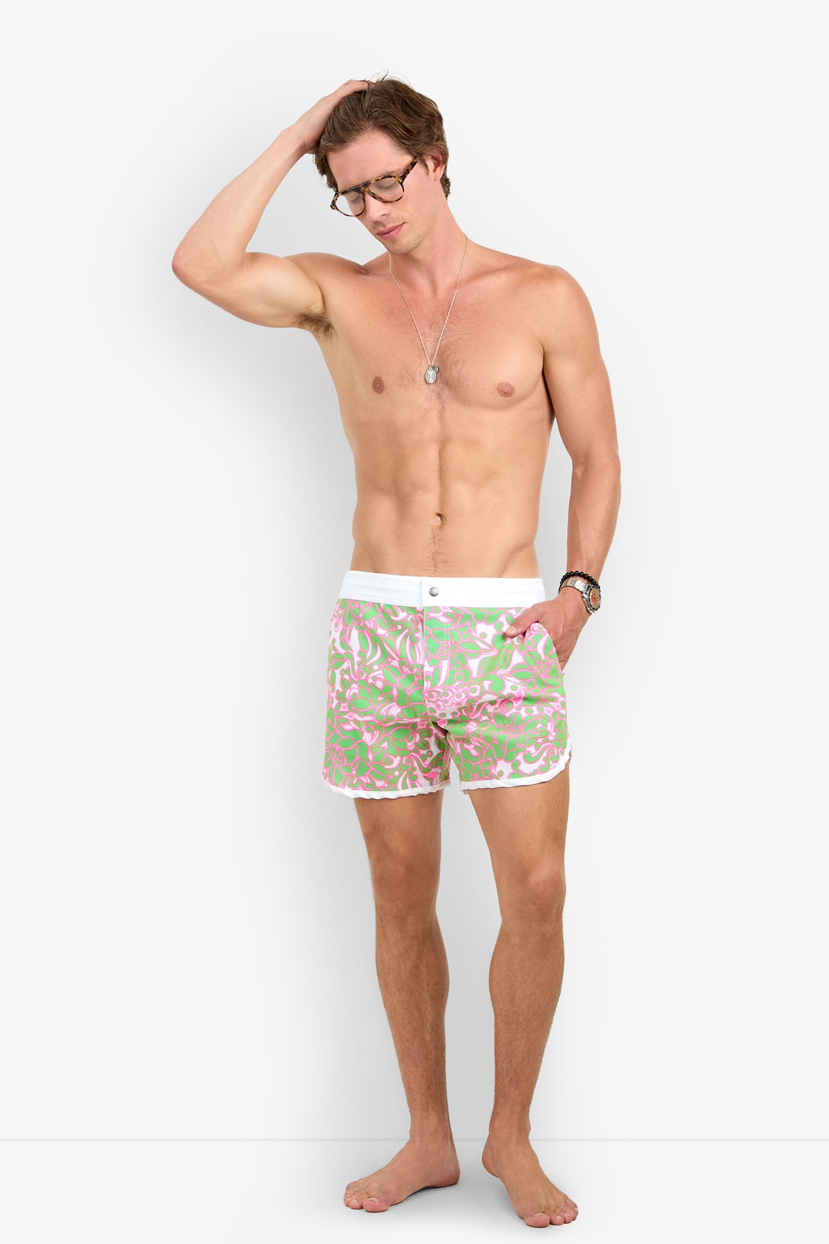 A shirtless man in glasses and Surfside Boardshort stands barefoot against a white background, one hand on his head and the other by his side.