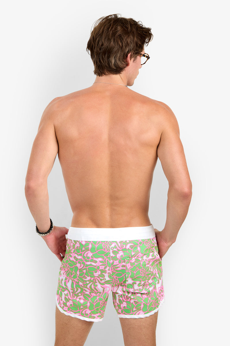 A shirtless man with brown hair faces away, wearing Surfside Boardshort in pink and green patterns with a white waistband, against a plain light background.