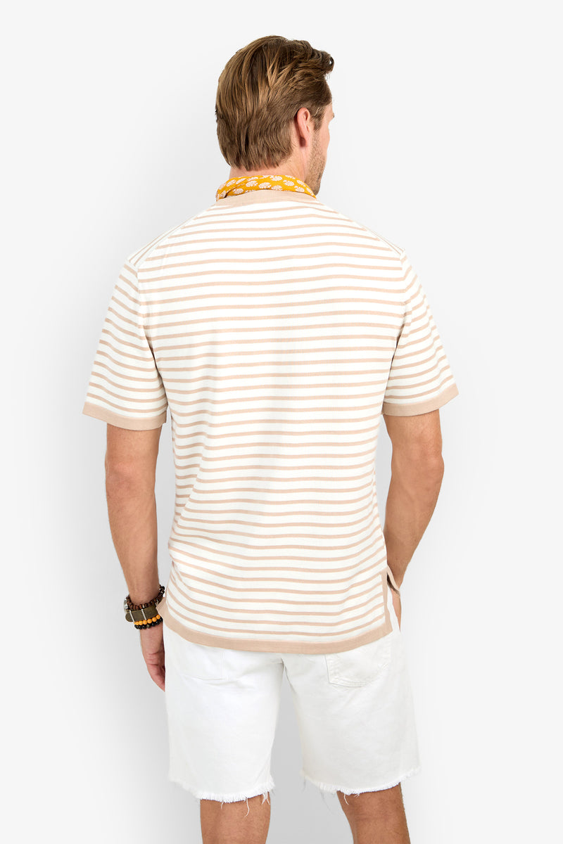 A man faces away, wearing the Giovanni Stripe Short-Sleeve Pullover in beige and white stripes, paired with white frayed shorts, bracelets, and a yellow beaded necklace against a plain white background.