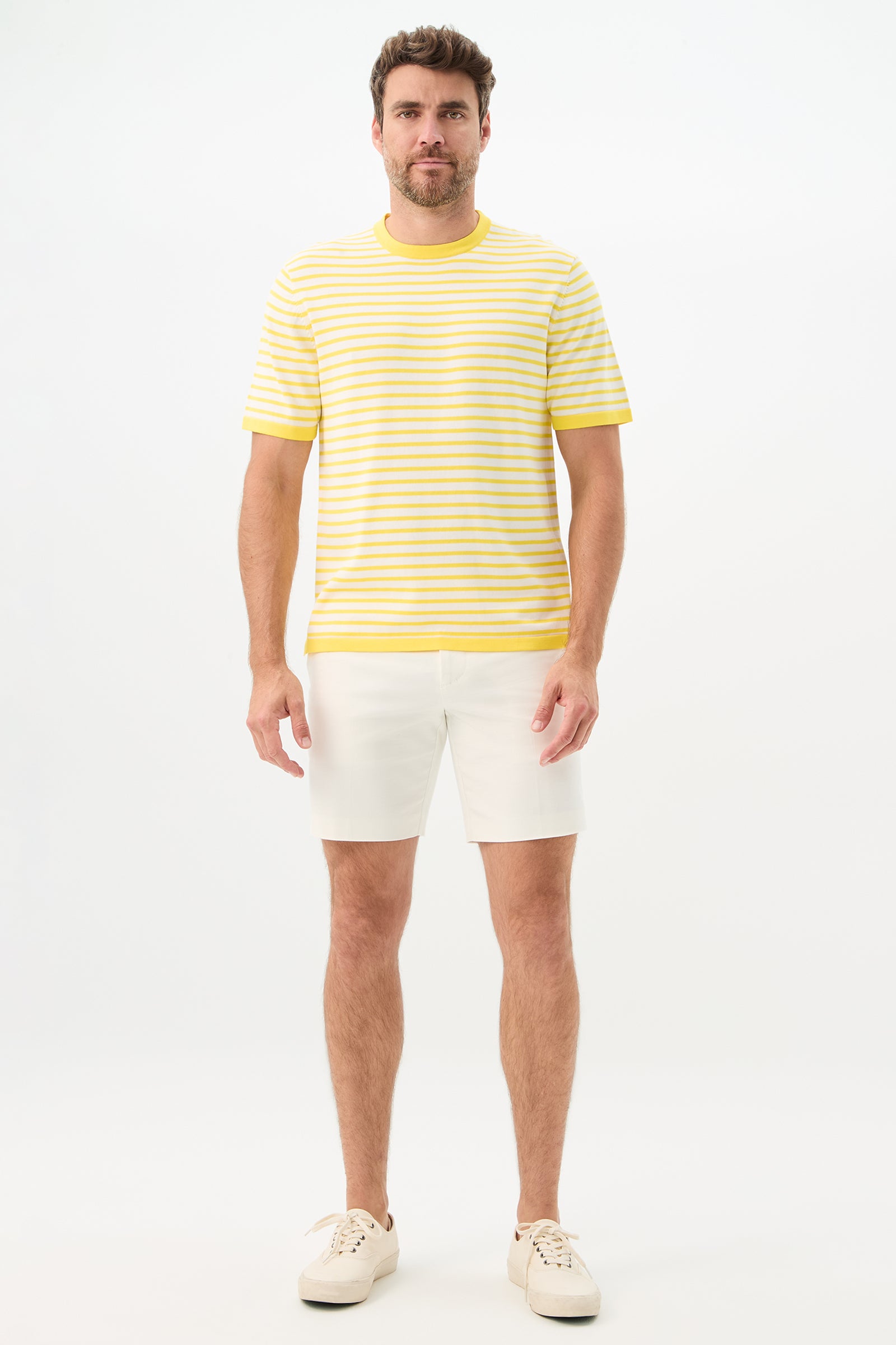 A man faces forward against a white background, wearing the Giovanni Stripe Short-Sleeve Pullover in yellow and white, paired with white shorts and sneakers.