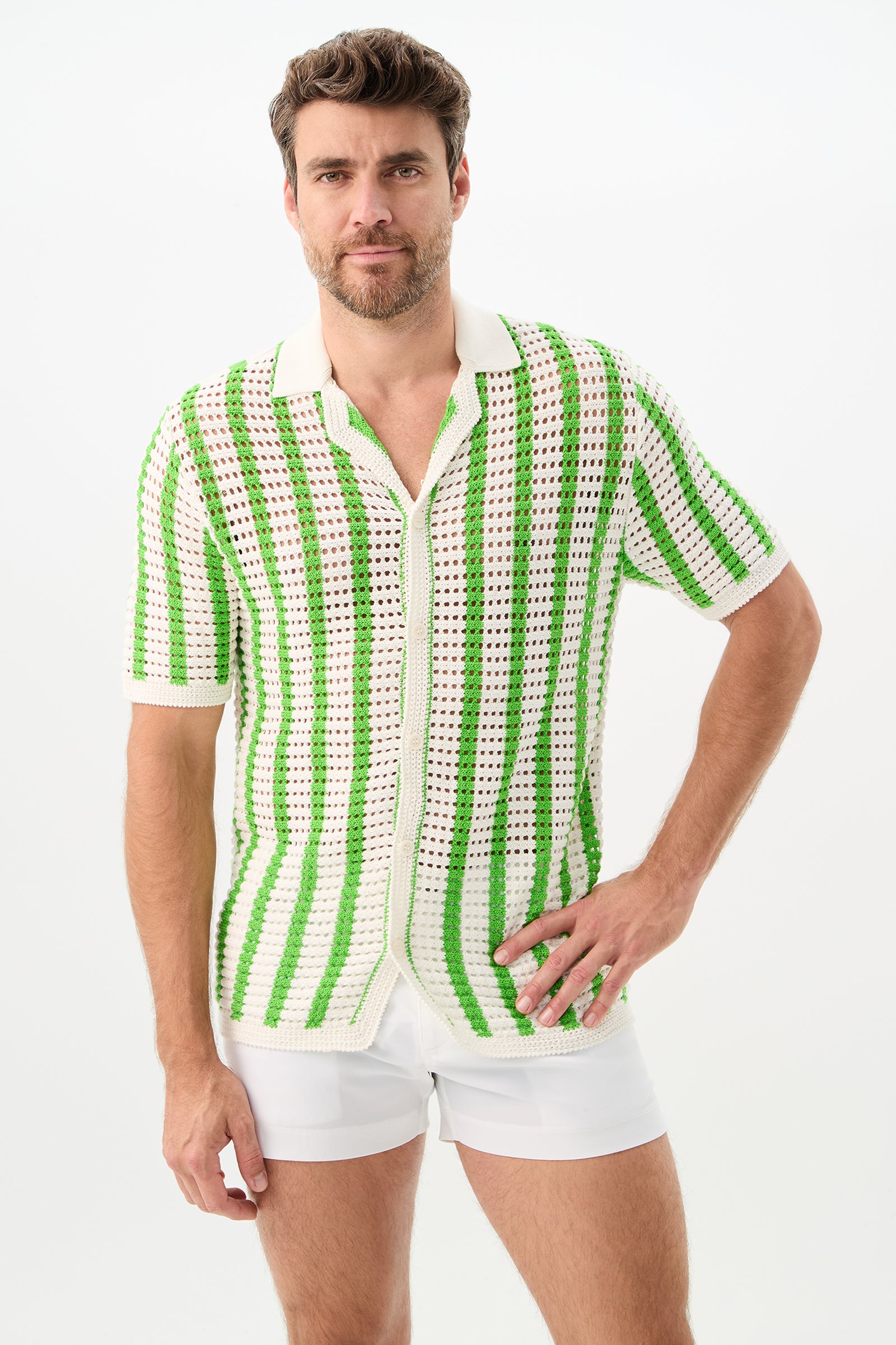 A man with short brown hair and a beard models the Easton 2 Short-Sleeve Shirt in Serene Green/Whitewash, paired with white shorts, standing against a plain white background with one hand on his hip.