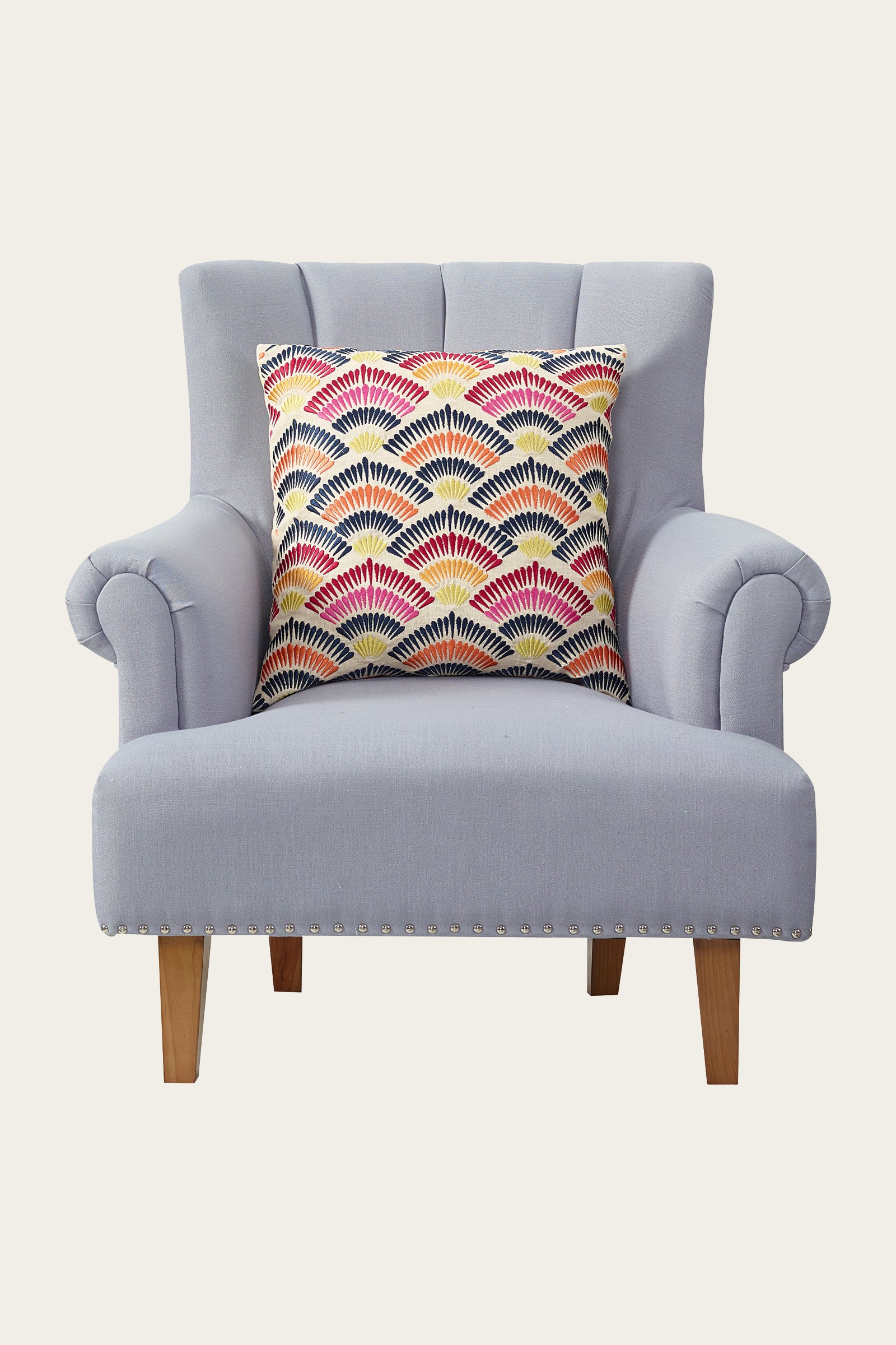 A light gray upholstered armchair with wooden legs and the Pasadena Embroidered Euro Throw Pillow—multi-colored with red, yellow, navy, and white fan-shaped patterns.