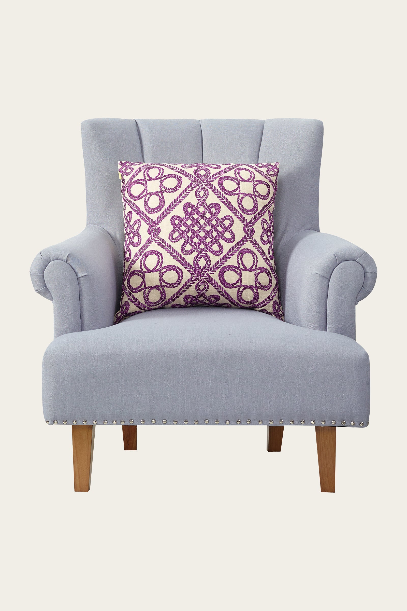 A light gray upholstered armchair with wooden legs, featuring the Costa Mesa Embroidered Euro Throw Pillow in multi, which showcases a central purple and white intricate geometric pattern.