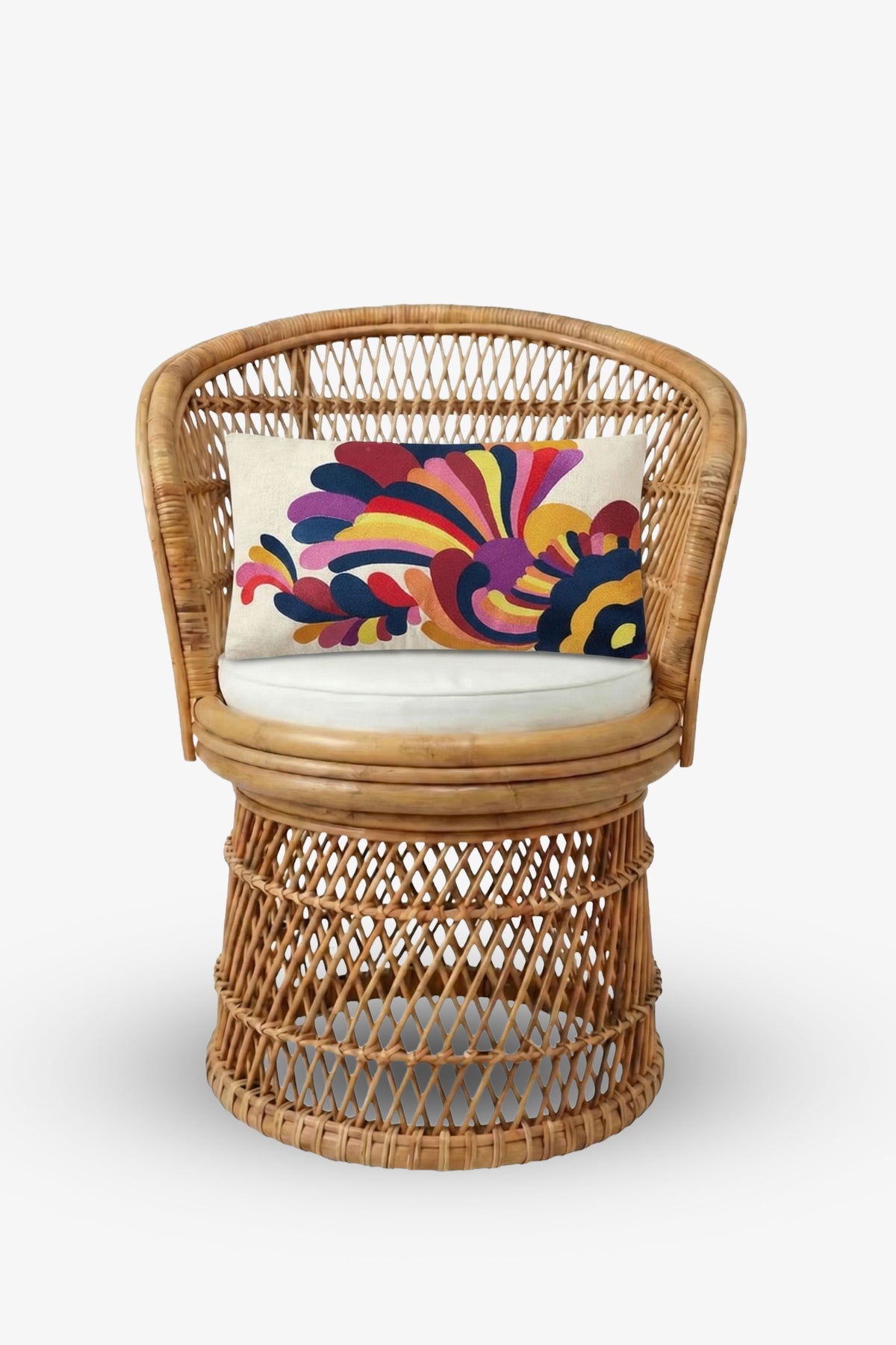 A wicker chair with a round base and a white cushion, featuring an Embroidered Lumbar Pillow with a colorful abstract pattern in red, pink, purple, yellow, and blue tones.