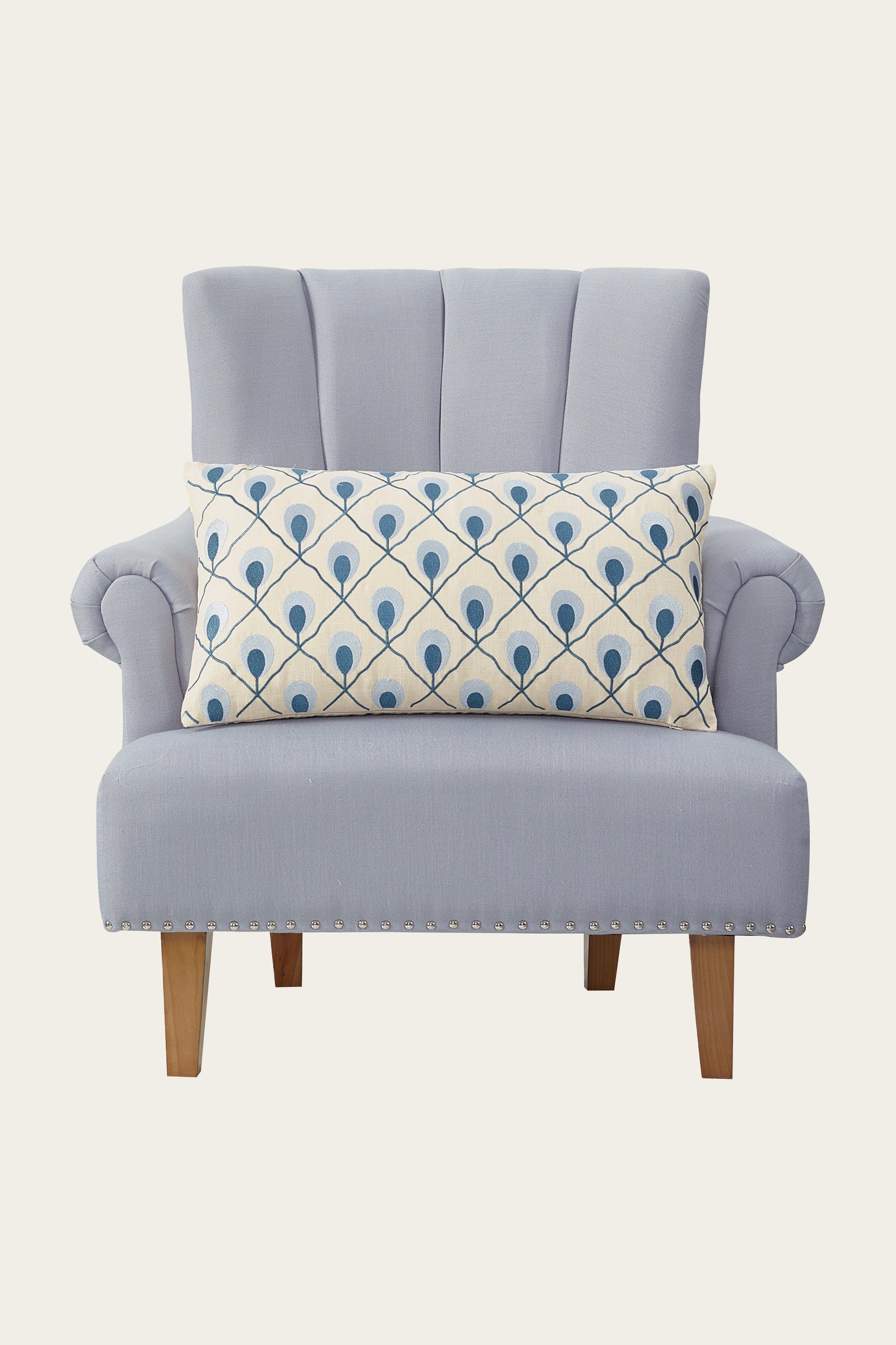 A light blue upholstered armchair with the Roseville Embroidered Throw Pillow - Terra, a large rectangular cushion, stands on wooden legs against a plain background.