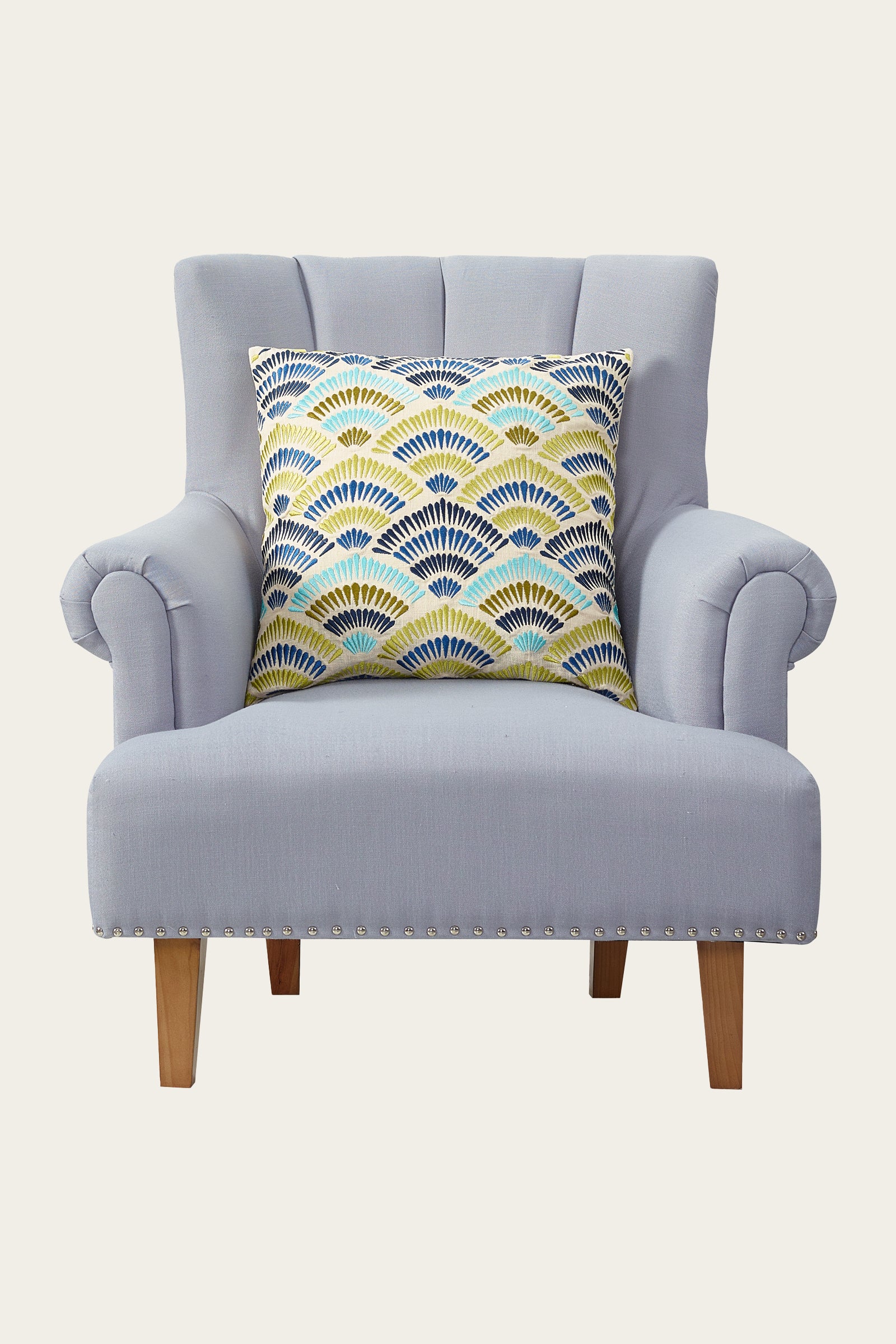 A light gray armchair with wooden legs and silver stud detailing, featuring the Pasadena Embroidered Euro Throw Pillow in blue.