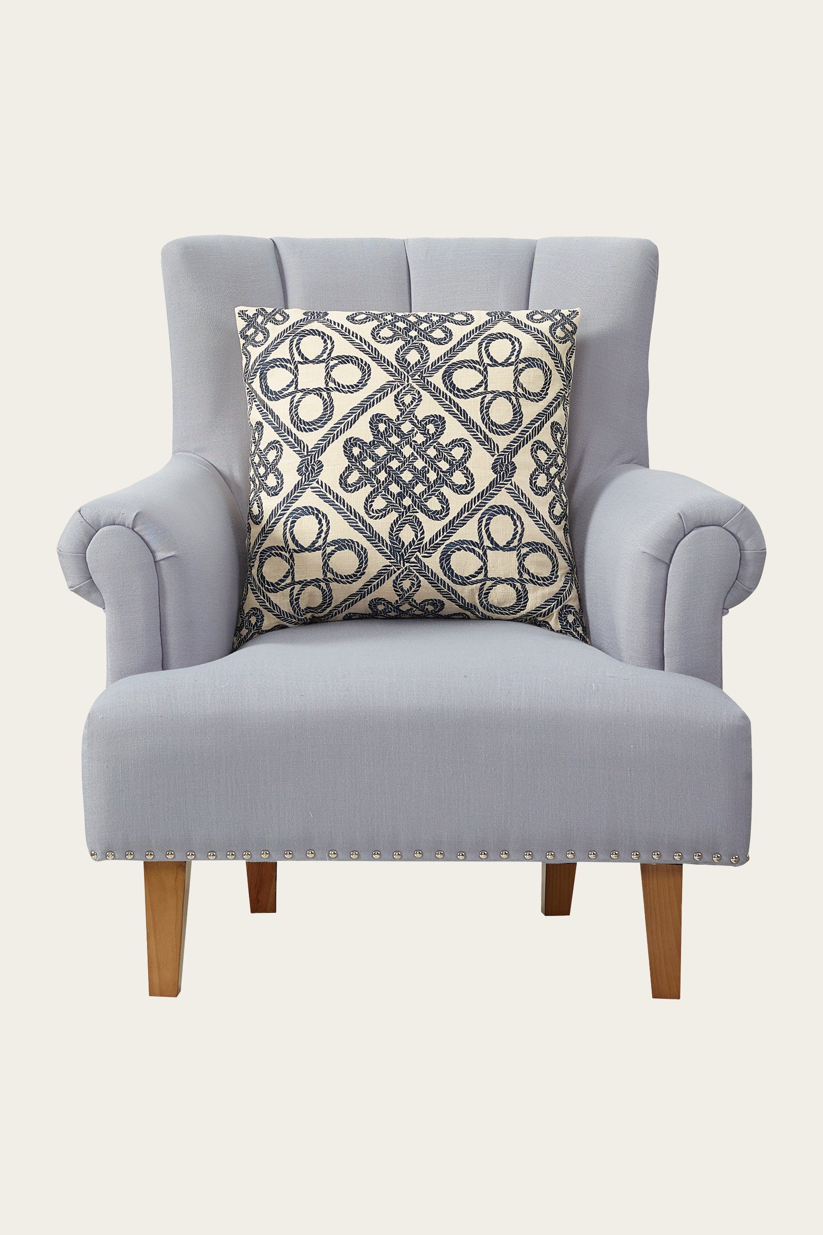 A light gray upholstered armchair with wooden legs and a studded trim, featuring the Costa Mesa Embroidered Euro Throw Pillow in blue with a navy and beige geometric pattern.