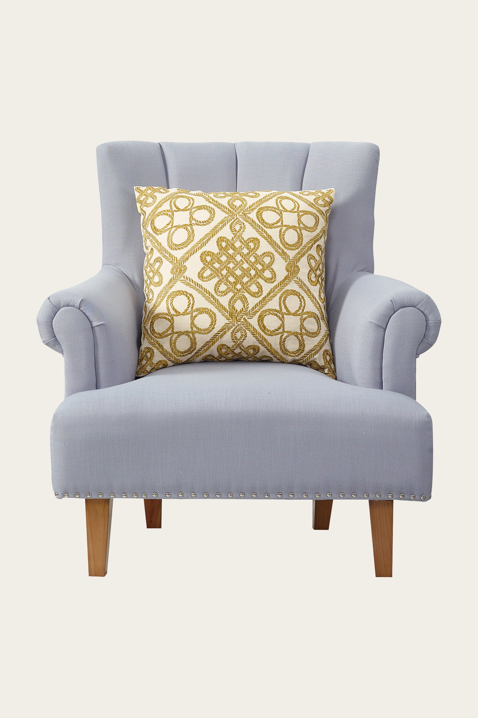 A light gray upholstered armchair with wooden legs and nailhead trim, featuring the Costa Mesa Embroidered Euro Throw Pillow in gold placed at the center of the backrest.