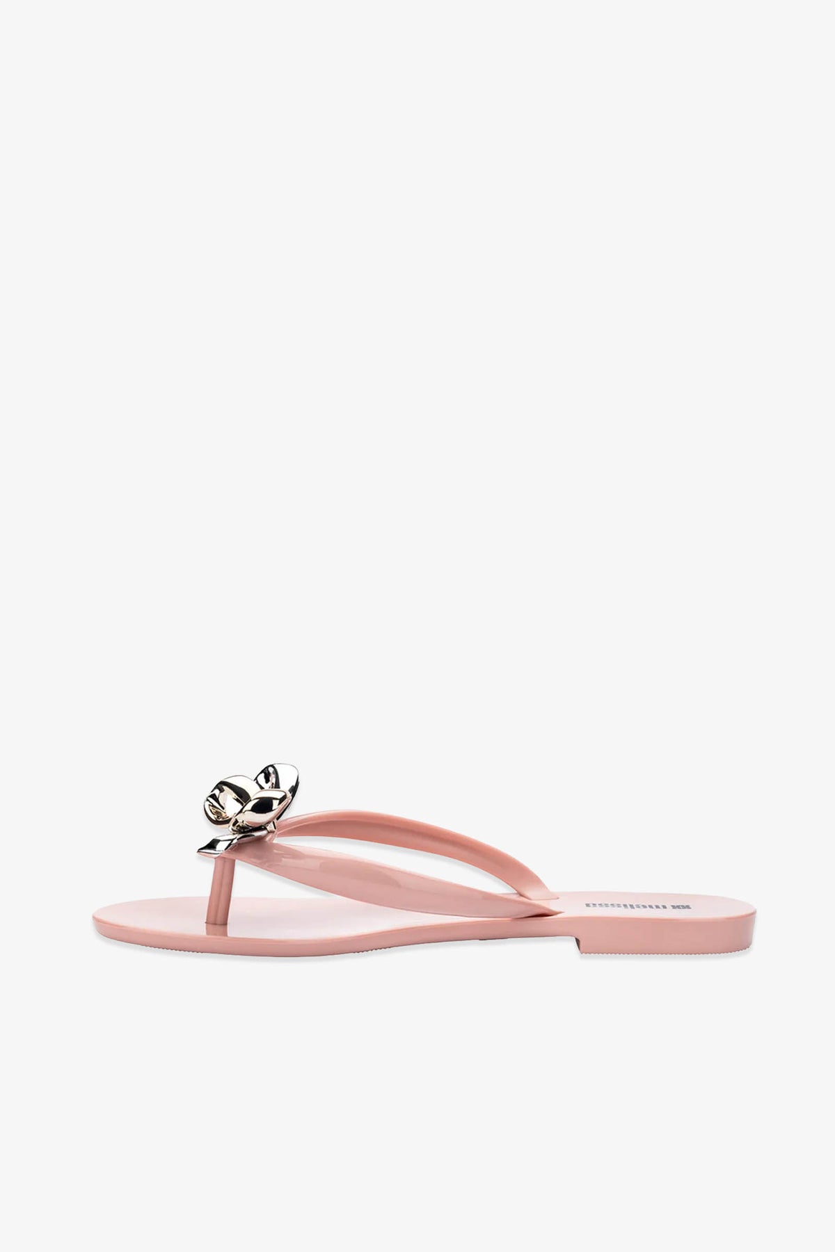 The Melissa Harmonic Eclipse Bow Sandal in pink features a shiny metallic flower decoration on the strap and is displayed on a plain white background.