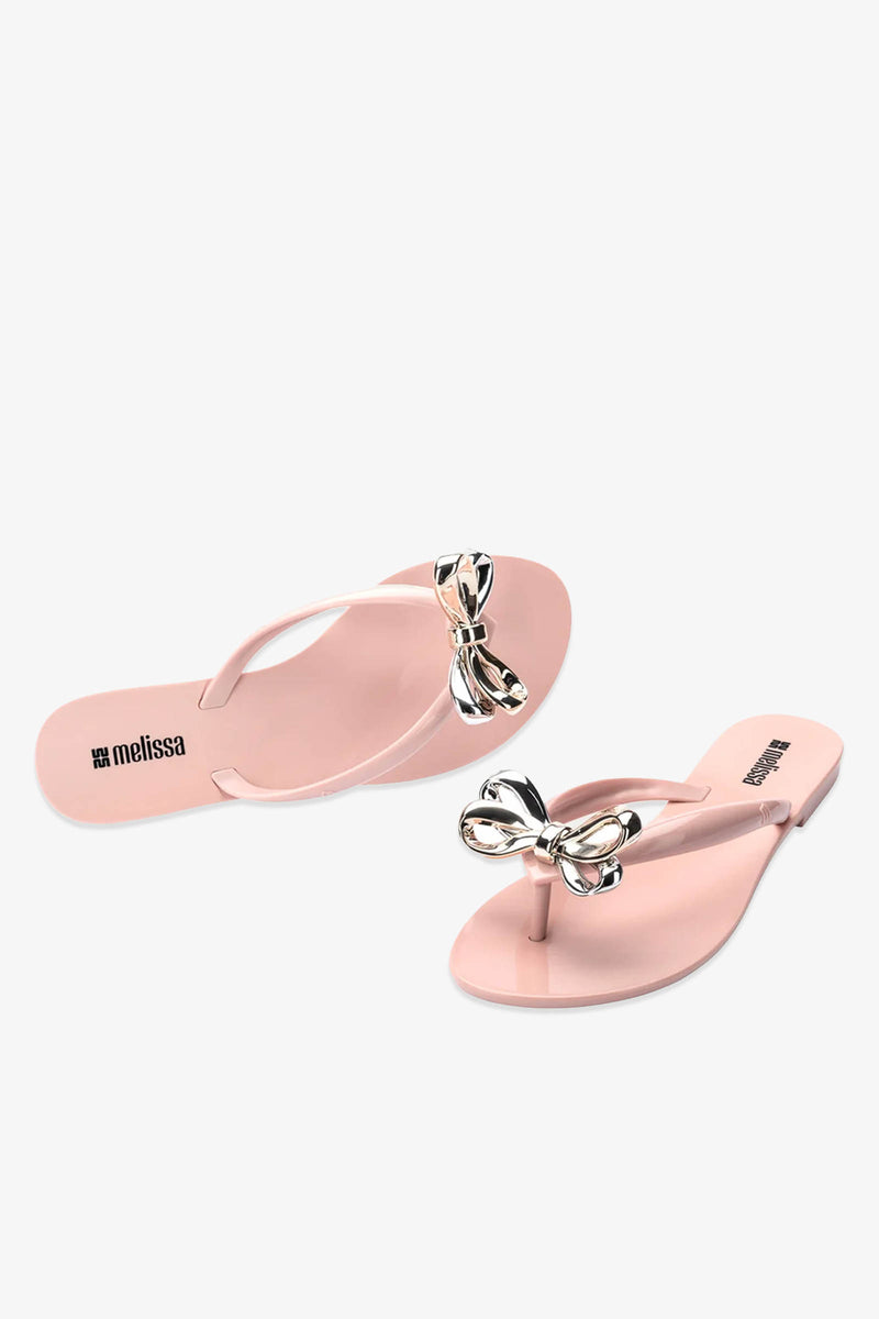 A pair of Melissa Harmonic Eclipse Bow Sandal in pink, featuring metallic bow decorations on the straps, displayed on a white background.