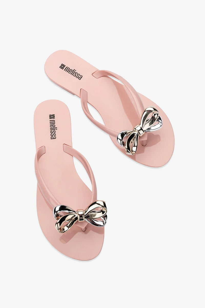 A pair of Melissa Harmonic Eclipse Bow Sandals in light pink, featuring metallic silver bows on the straps, displayed on a white background.
