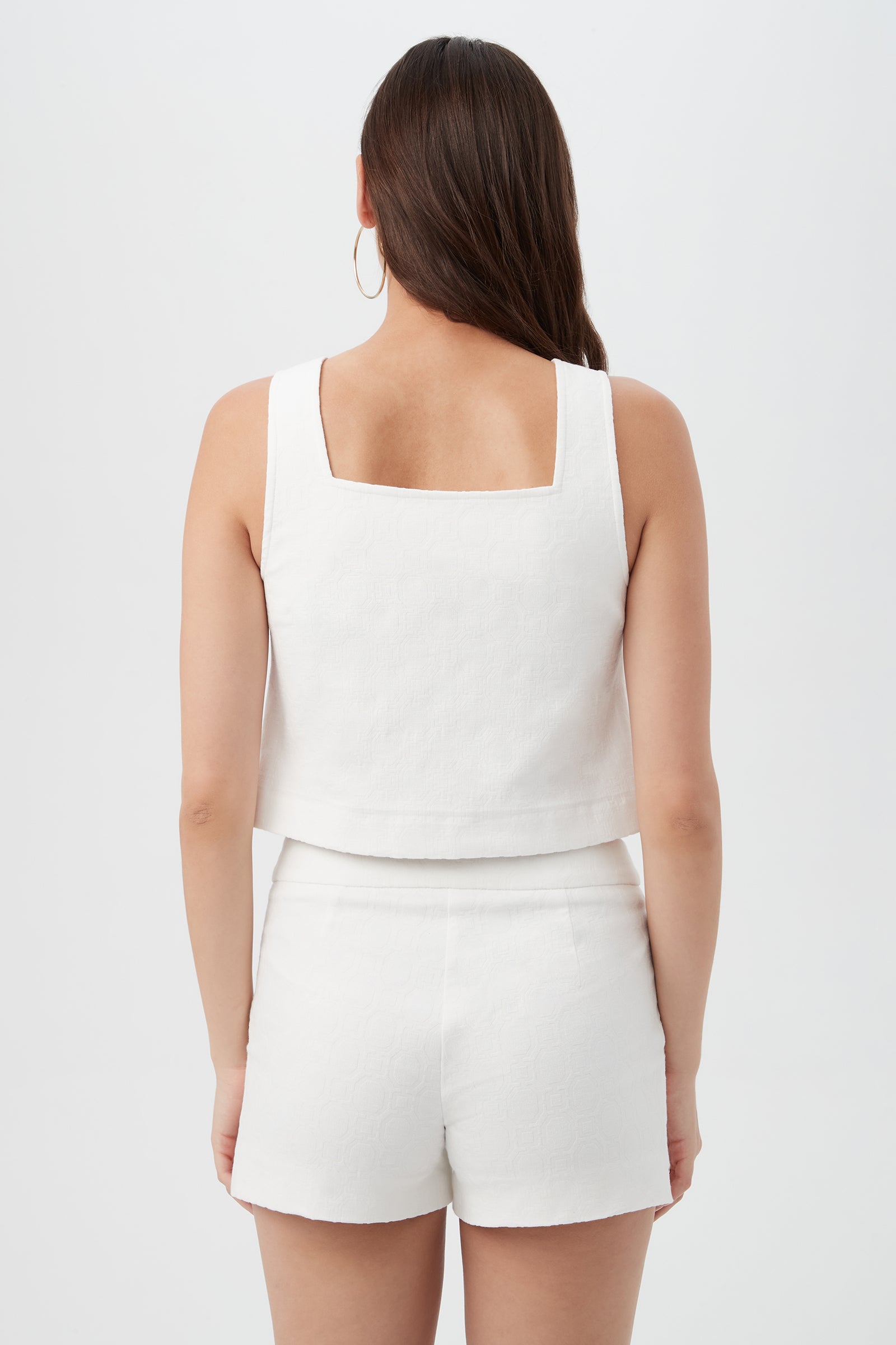 A woman with long brown hair, seen from the back, wears the Cherrey Top—a sleeveless white square-neck crop top—paired with matching high-waisted white shorts against a plain white background.