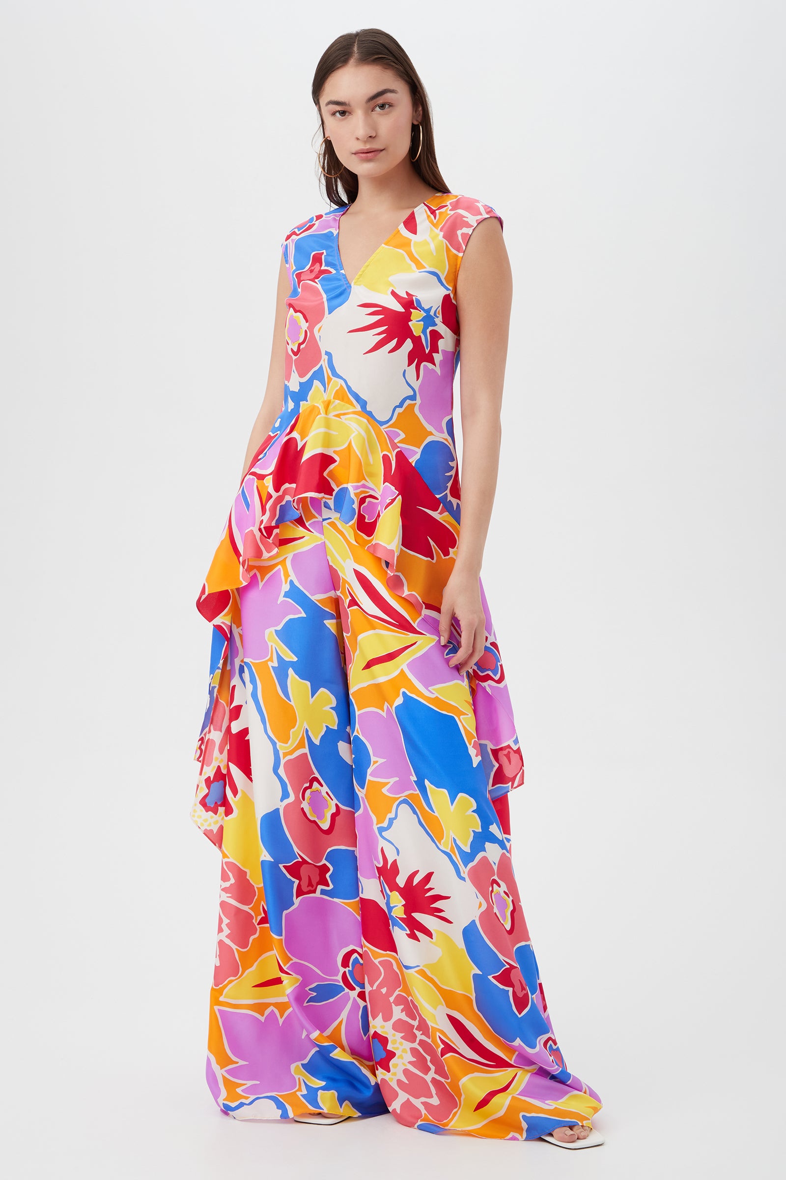 A woman models the Jack Wide-Leg Pant - Soie Paradis, featuring a vibrant abstract floral print in red, yellow, pink, blue, and white. The flowy wide-leg pants stand out against a plain white background.