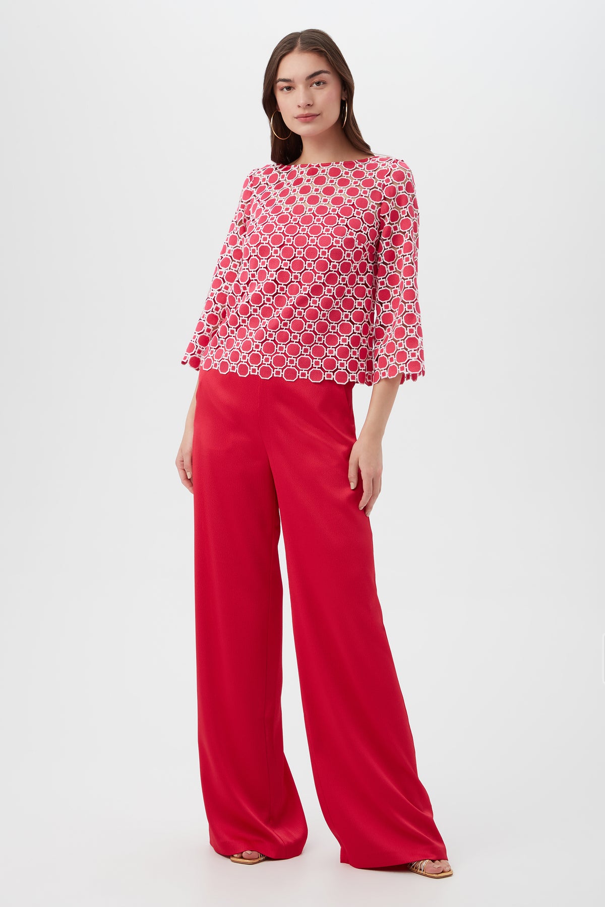 A woman stands against a white background wearing the Sun Top, which features red and white patterns with flared sleeves, paired with loose-fitting, high-waisted red pants. She has long, straight hair and neutral-colored shoes.
