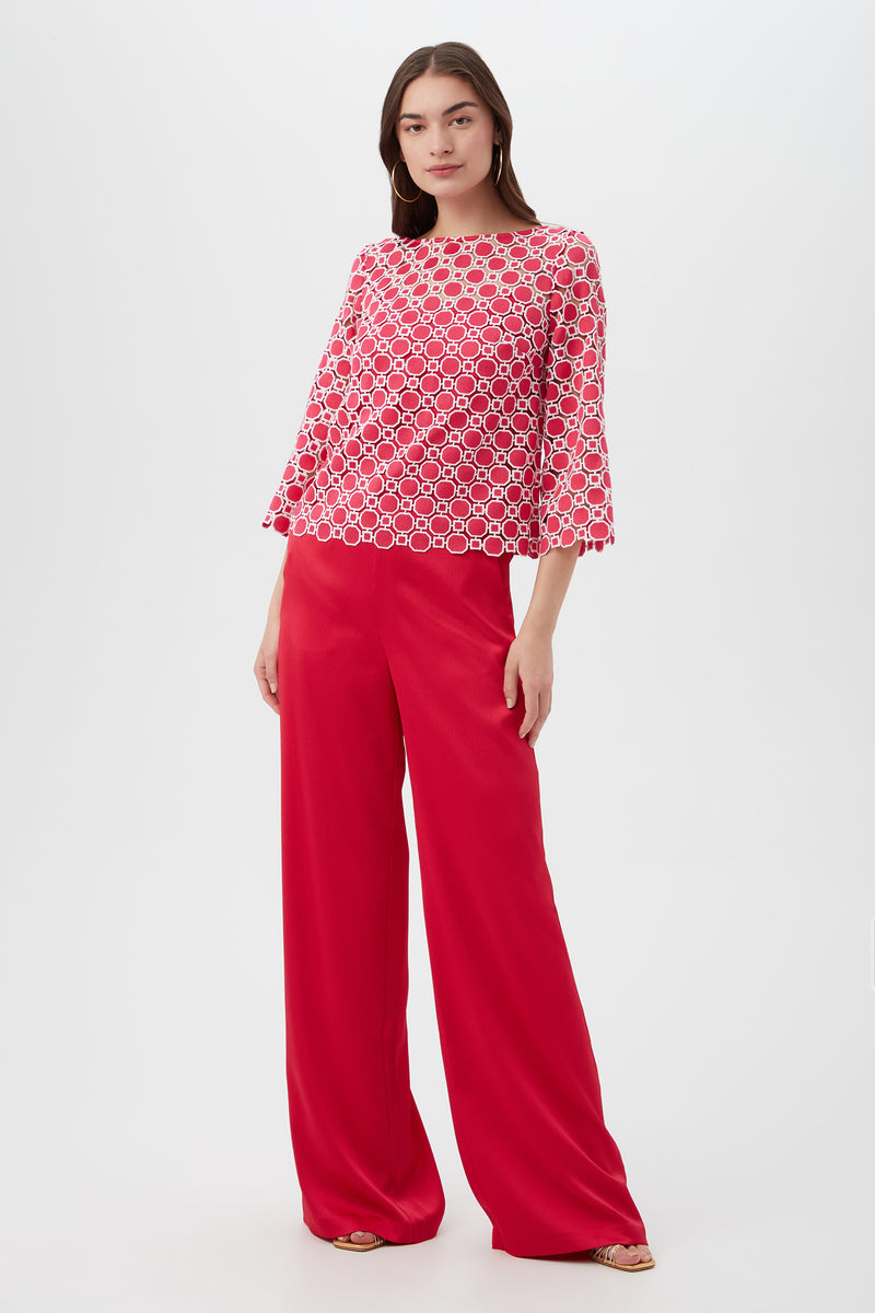 A woman stands against a white background wearing the Sun Top, which features red and white patterns with flared sleeves, paired with loose-fitting, high-waisted red pants. She has long, straight hair and neutral-colored shoes.