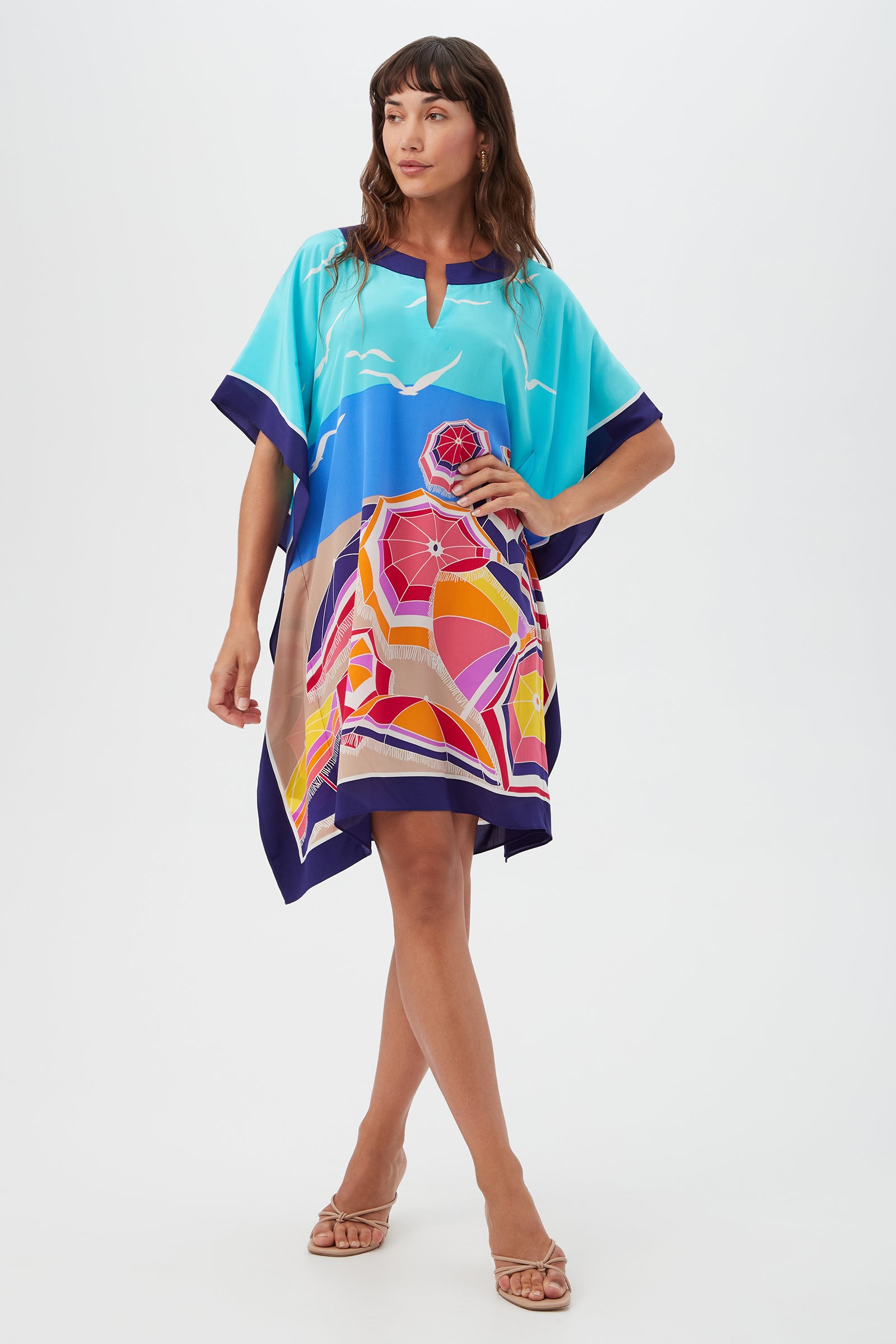 A woman poses barefoot against a white background in Theodora Caftan Dress - Parapluie Silk, a loose multi-colored silk dress with abstract geometric and landscape designs.
