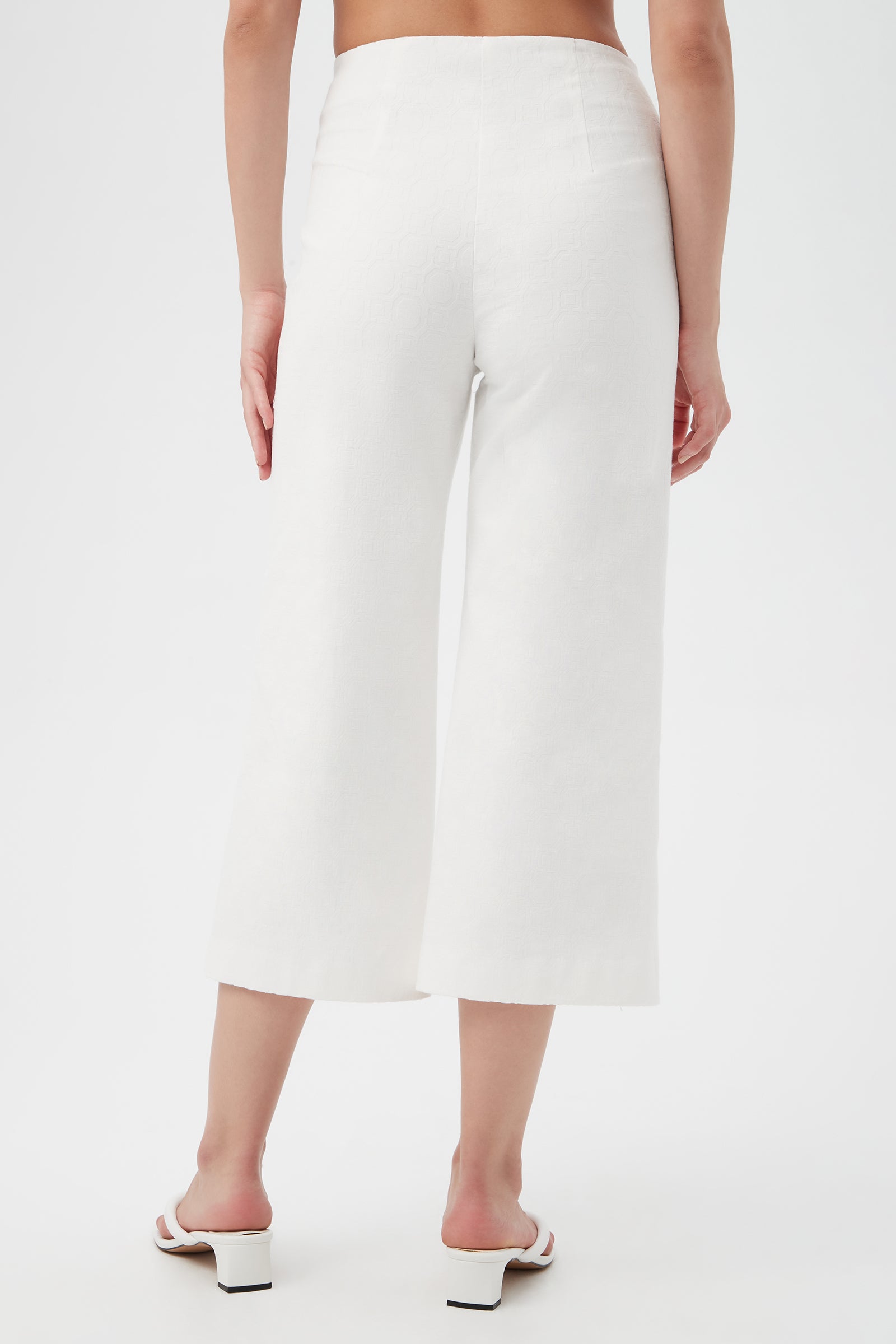 A person stands facing away against a plain background, wearing Saltie 2 Crop Pants and white heeled sandals.